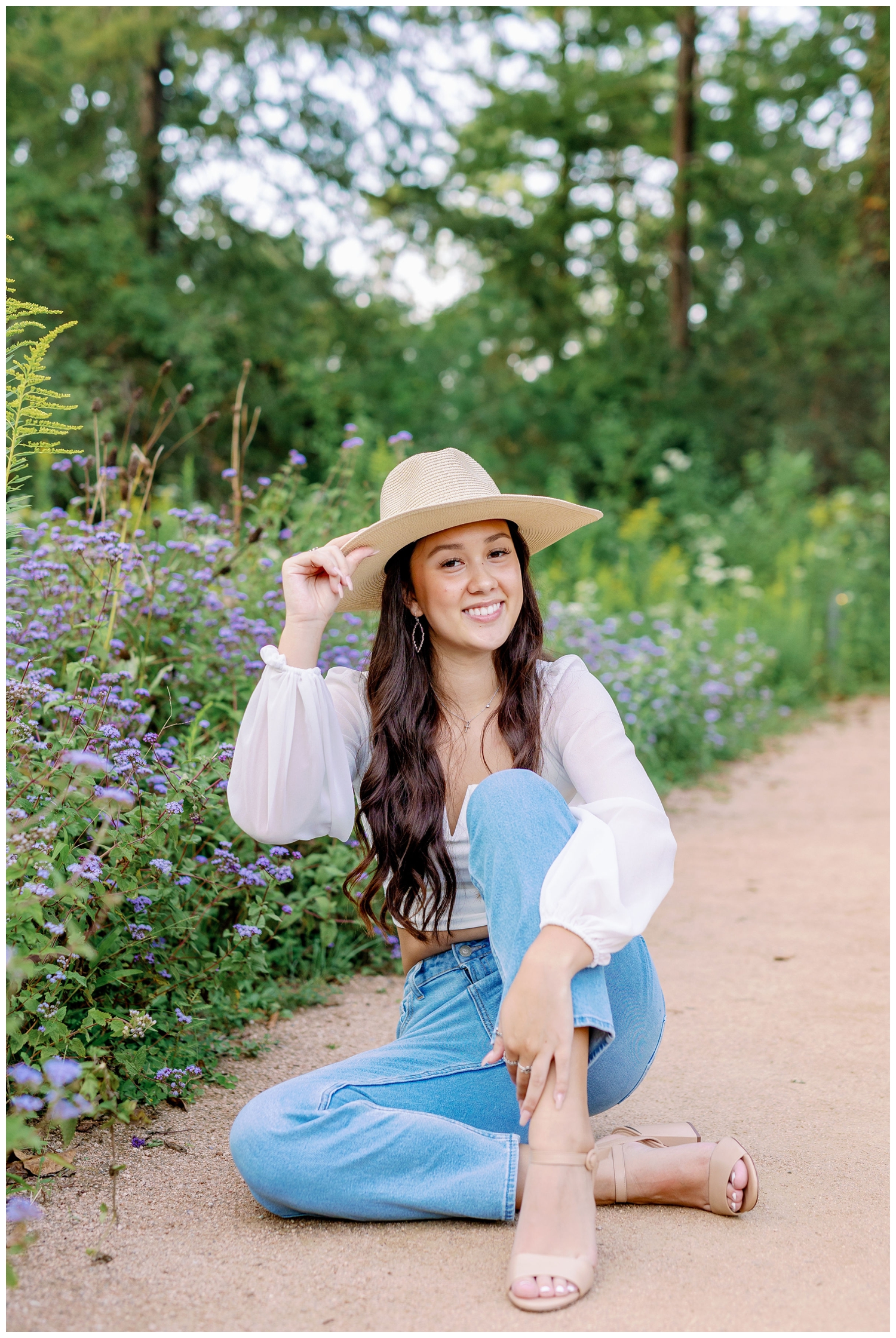 girl sitting in front of purple and yellow flowers holding hat on her head fall senior pictures Houston Arboretum