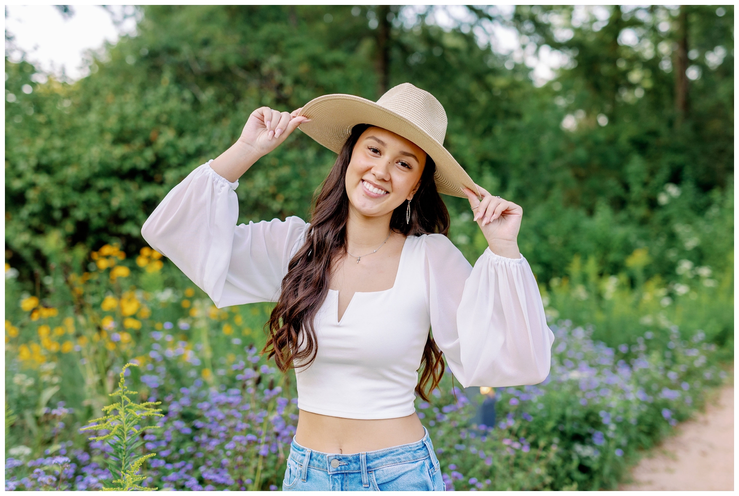 girl in white shirt and jeans standing and holding her hat at Arboretum fall senior pictures Houston