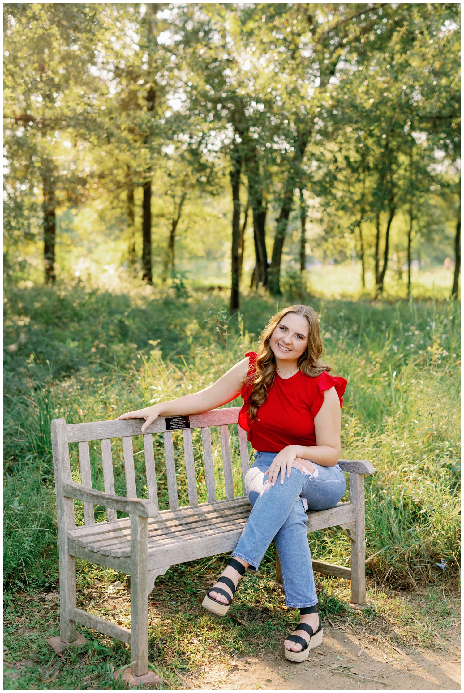 girl in jeans and red shirt sitting on bench for senior pictures Houston Arboretum