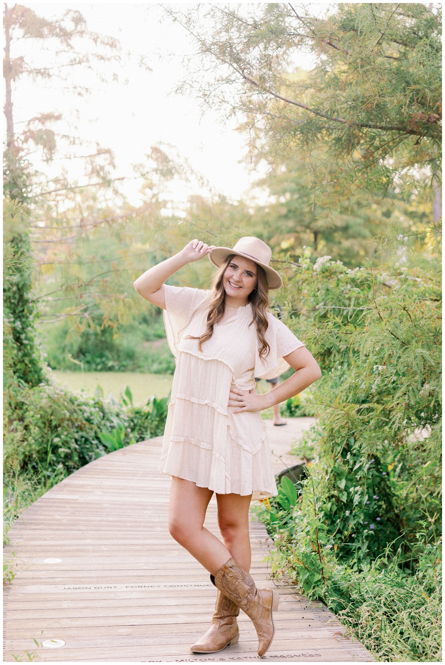 girl in cream sundress with cowboy boots and tipping cowboy hat senior pictures Houston Arboretum