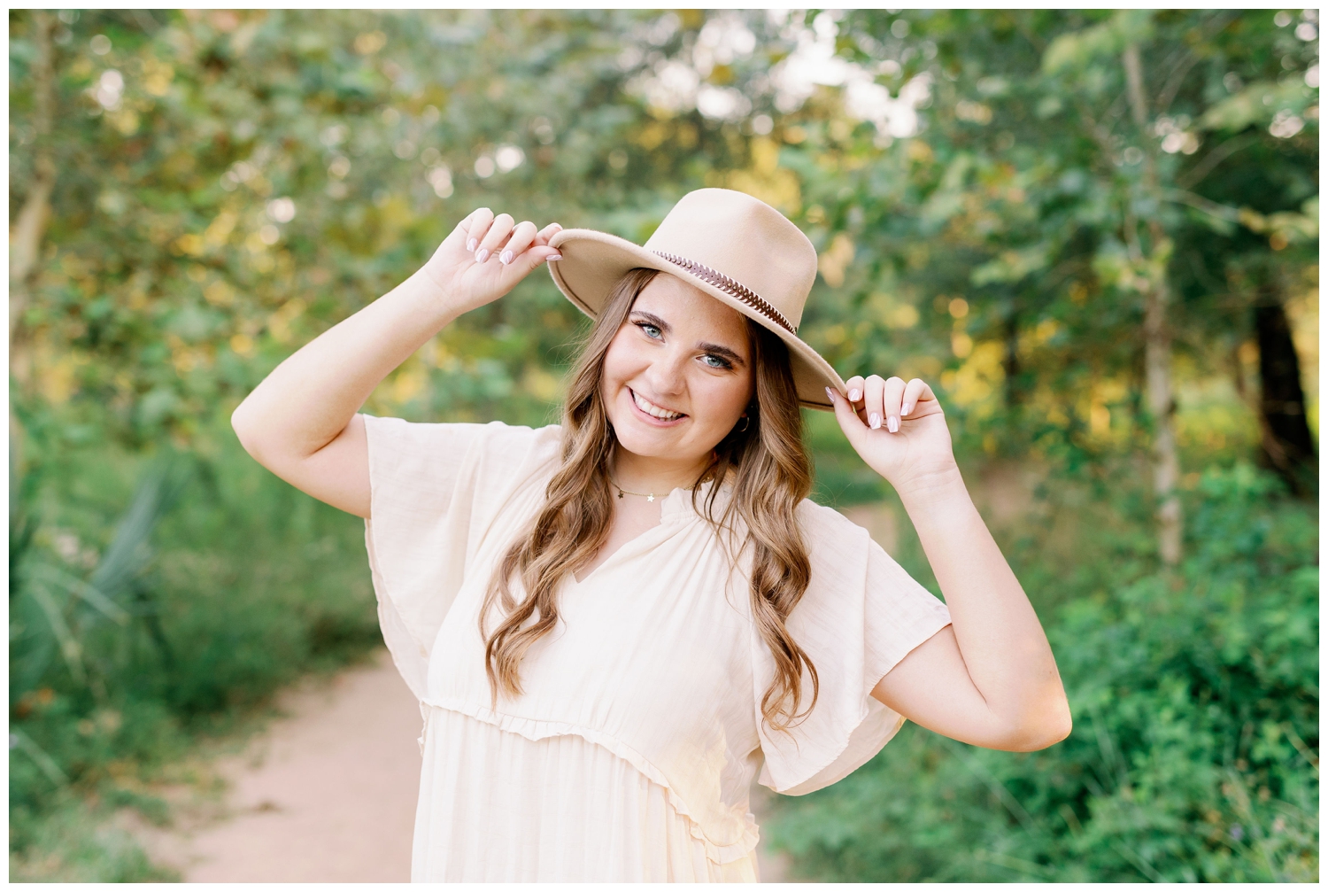 senior pictures Houston at Arboretum with girl in cream dress and both hands on cowboy hat