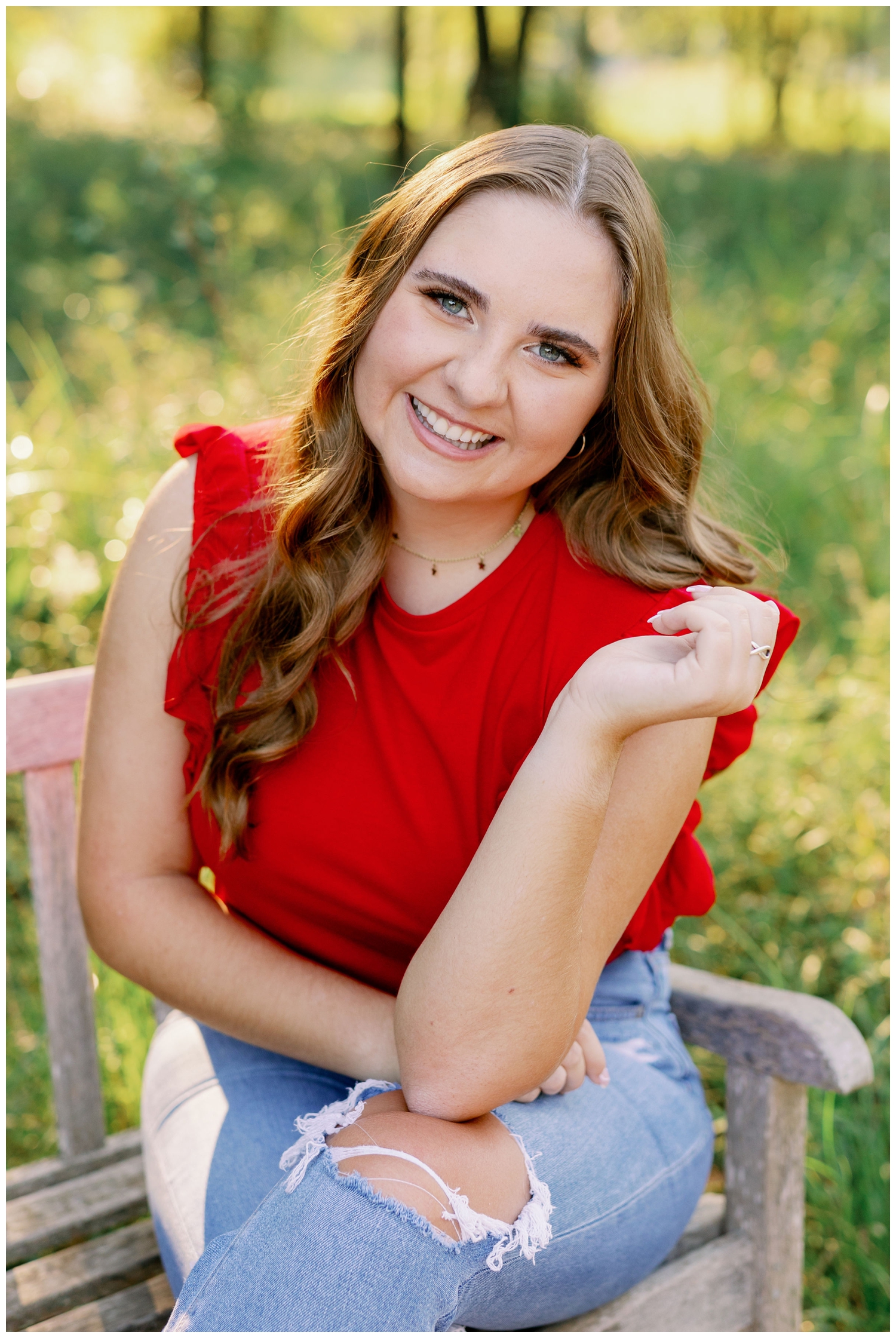 girl in jeans and red top sitting on bench inside Houston Arboretum for senior pictures Houston