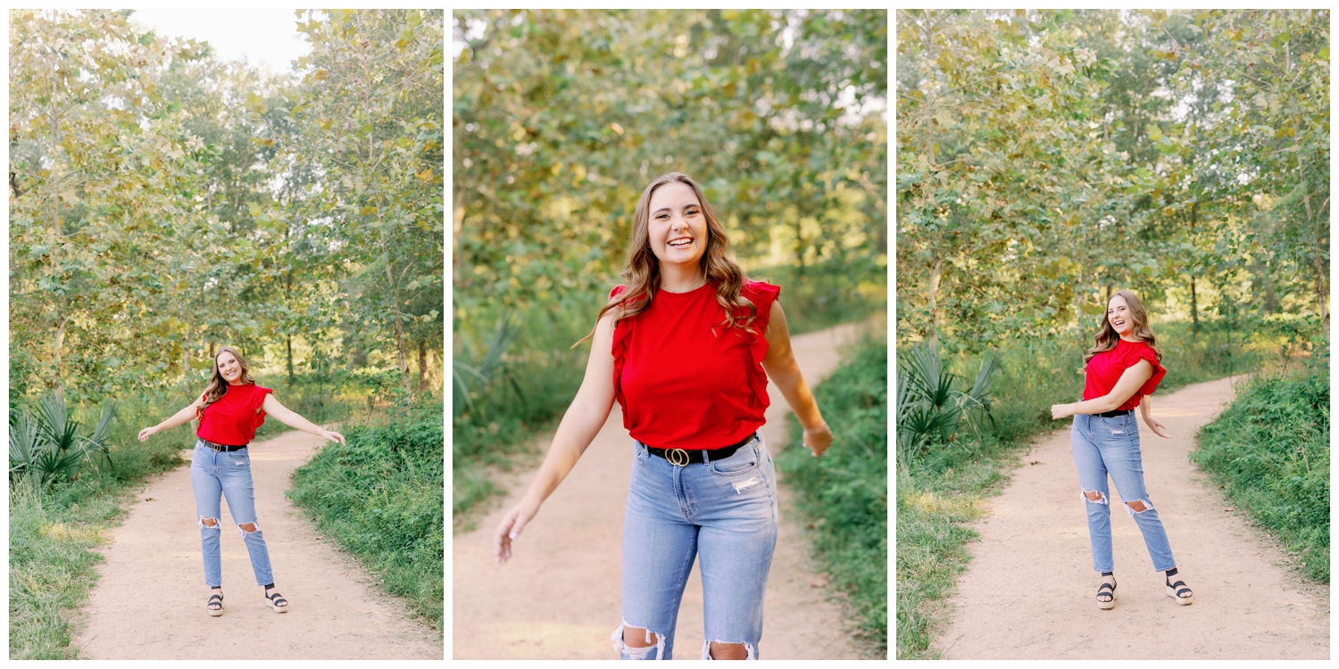 girl spinning on pathway for senior pictures Houston Arboretum wearing jeans in red blouse