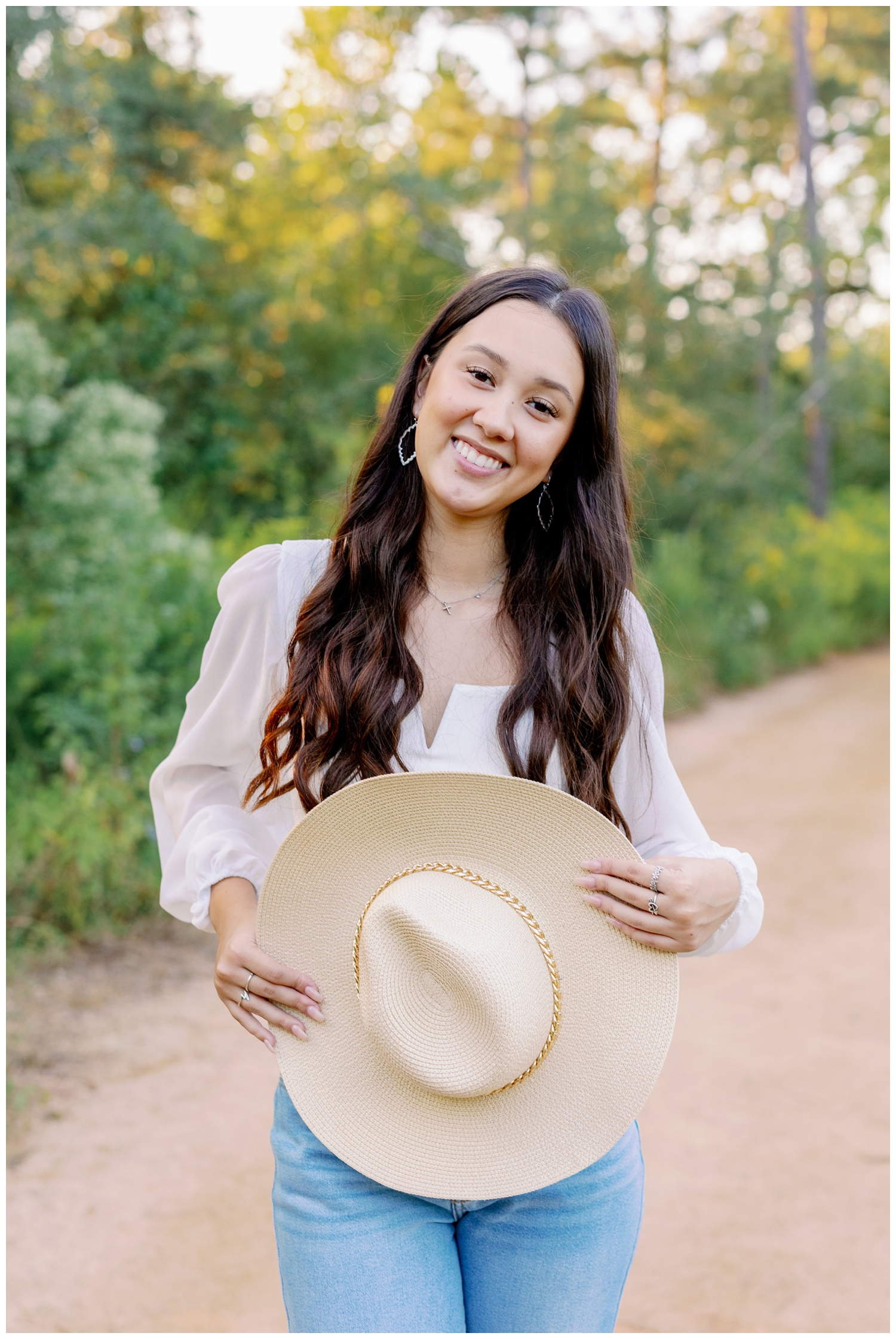 girl smiling in front of trees and holding cowboy hat