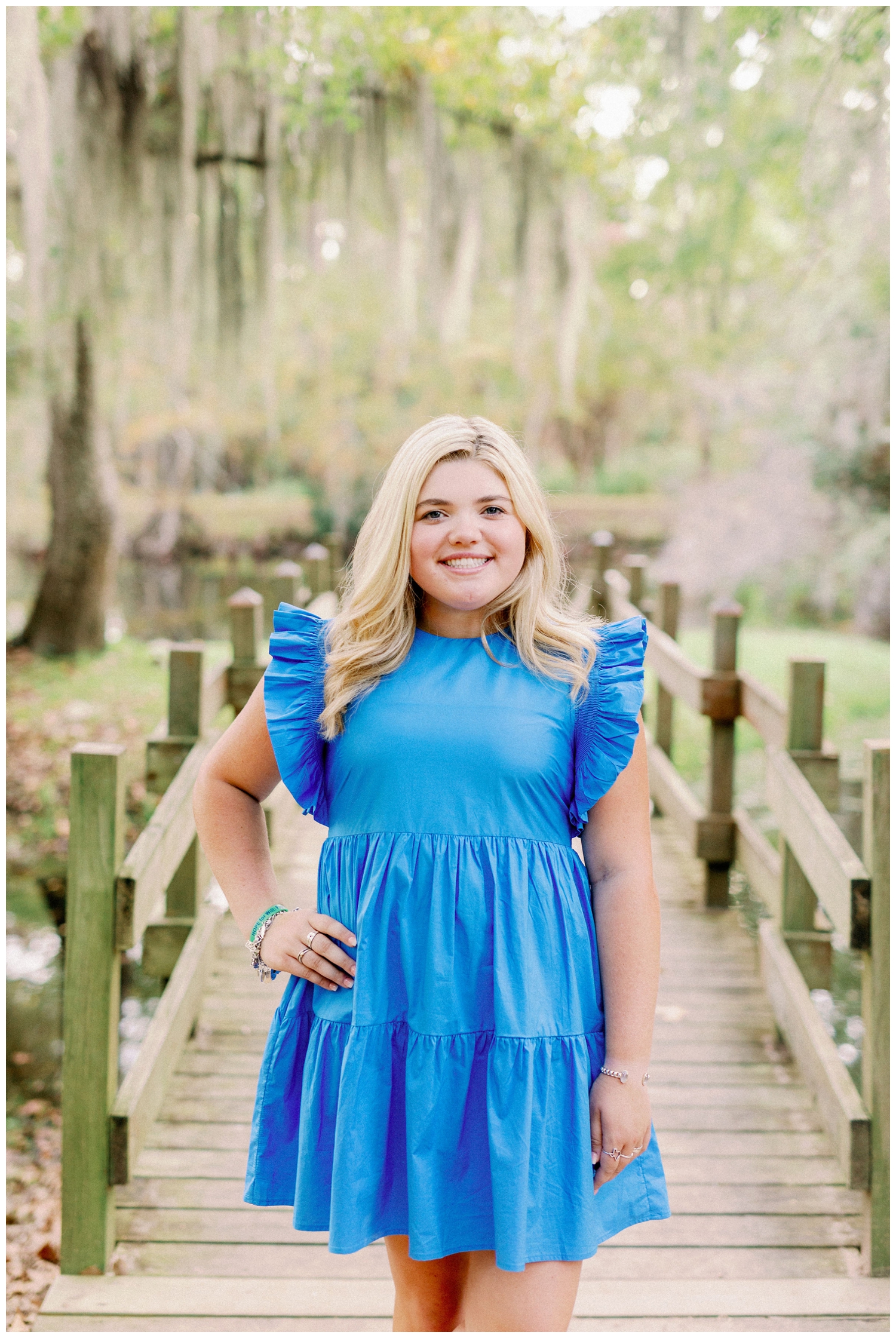 girl standing on bridge in bright blue dress under mossy tree at Cy-Hope for colorful Houston senior photography