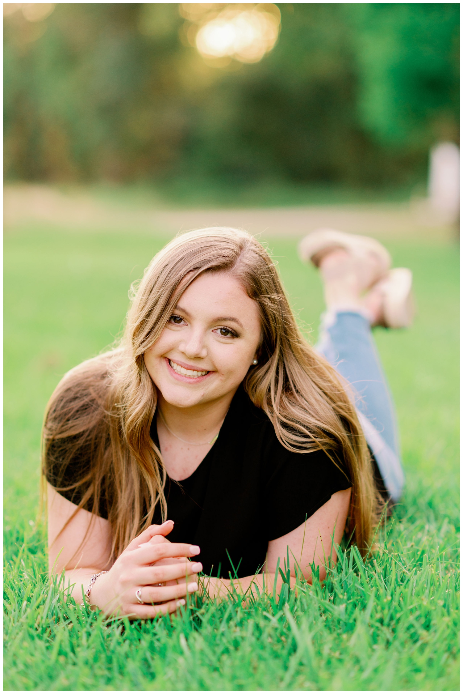girl laying on grass in black shirt and jeans on lawn at Cy-Hope Cypress