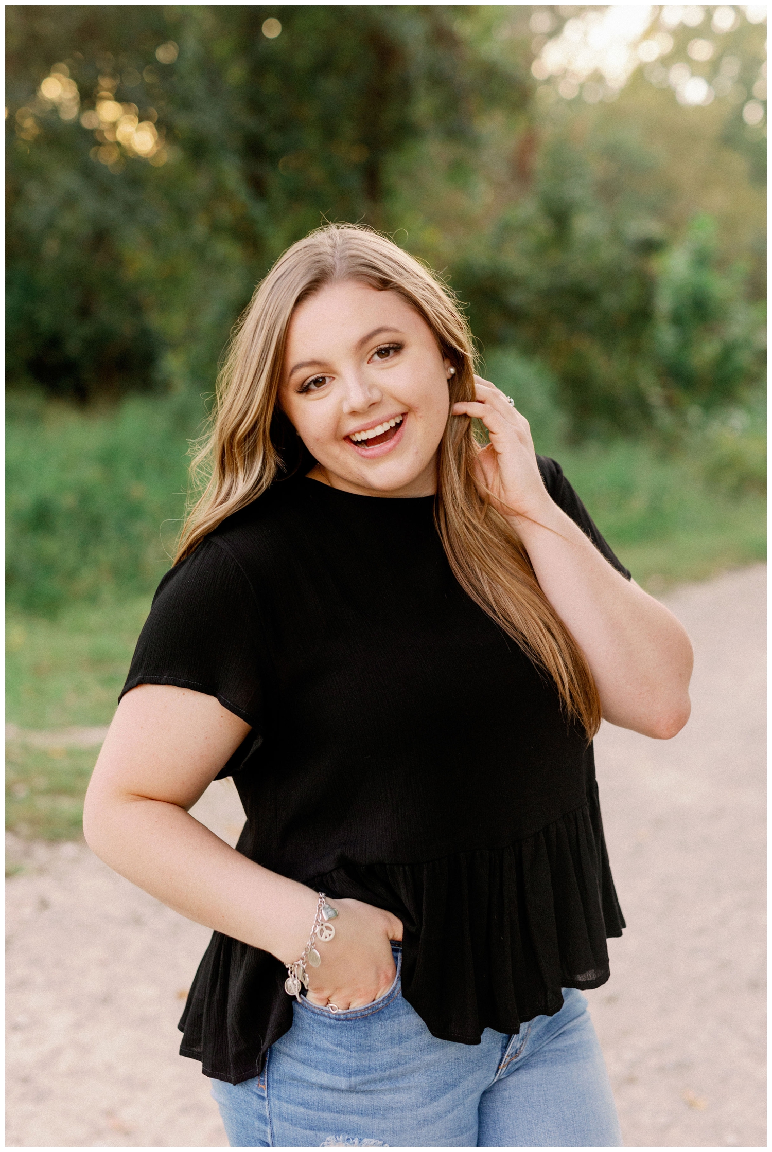 girl in in black shirt with hand in hair standing on pathway Cypress senior photography