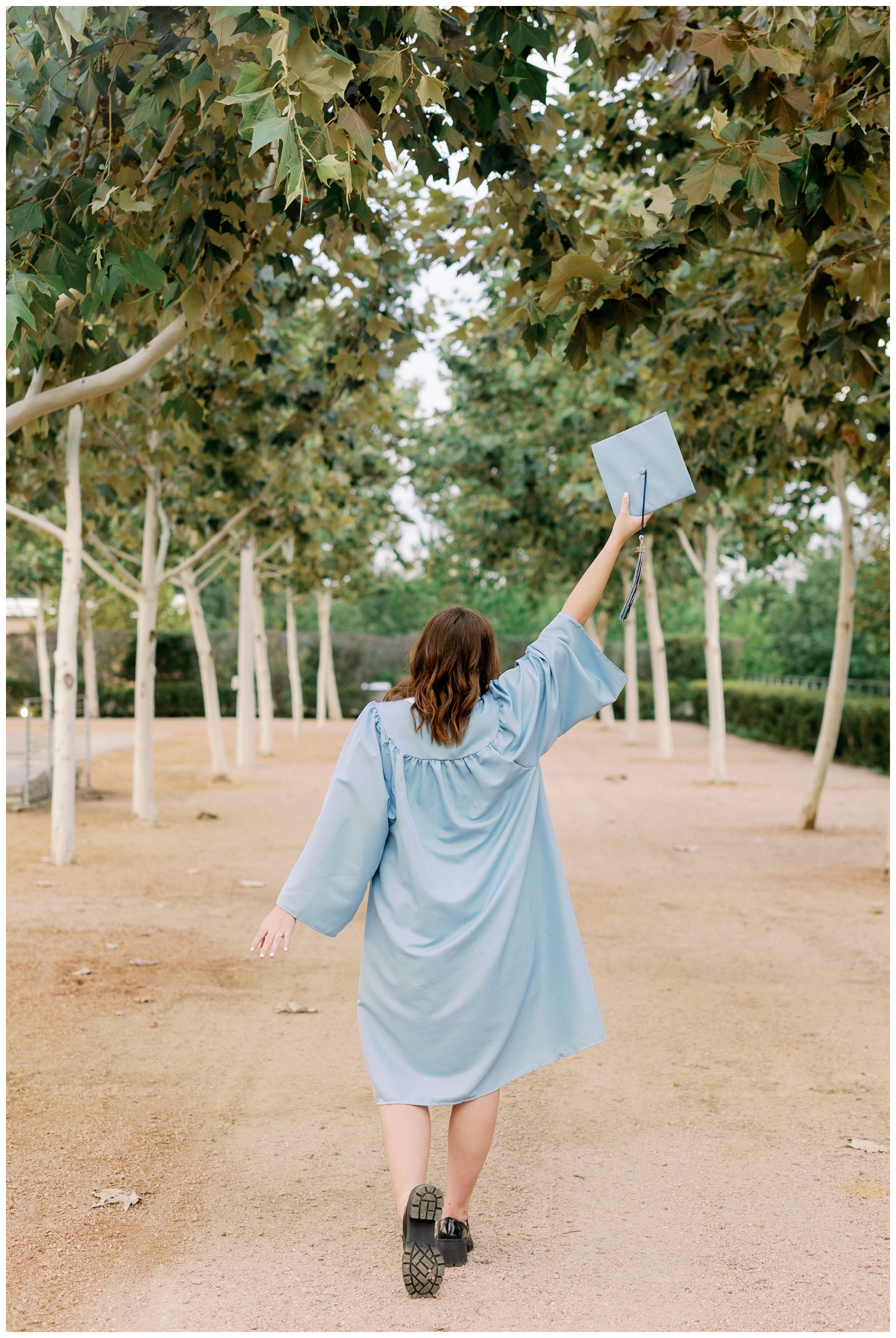 girl walking away from camera holding graduation cap in the air