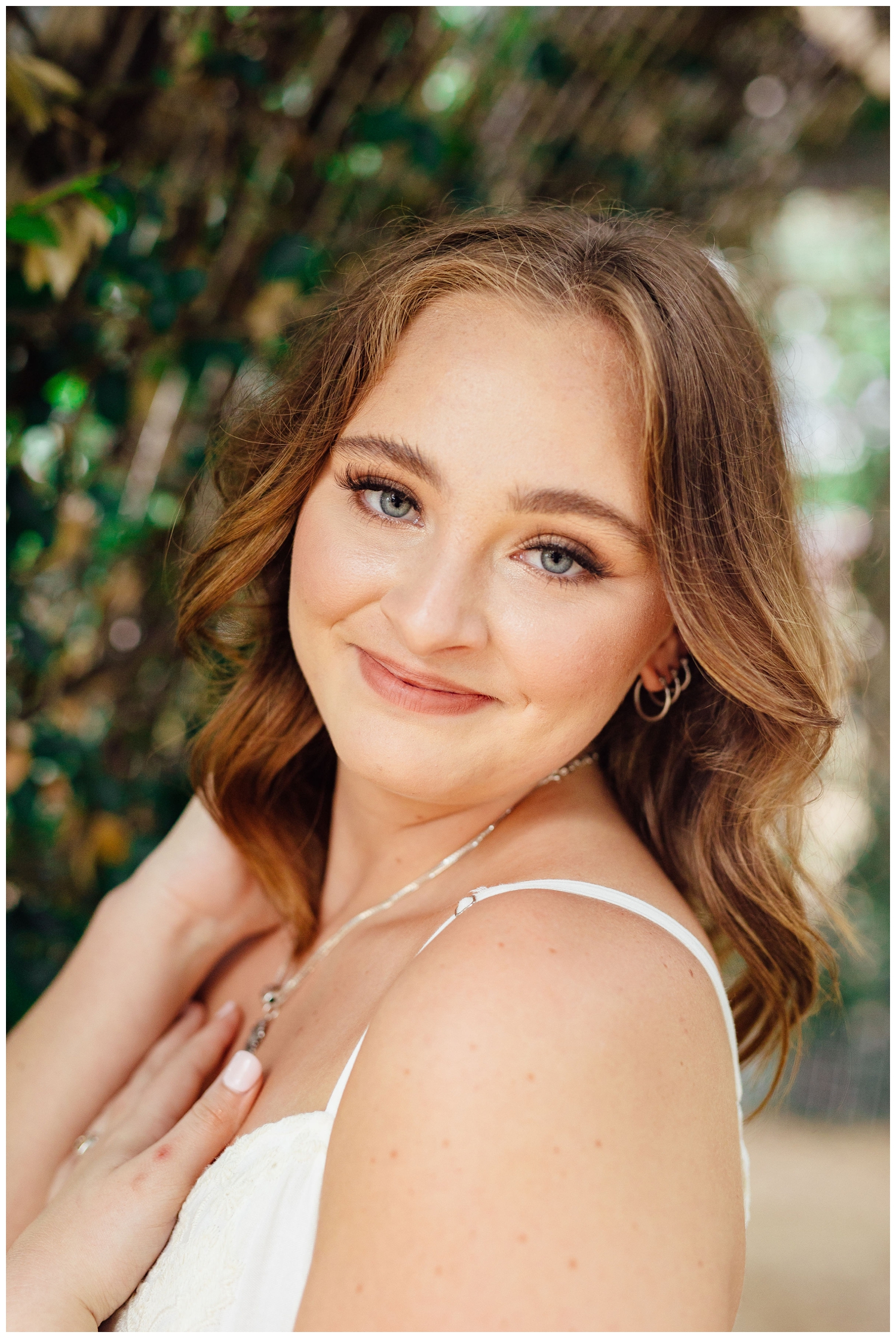 girl smiling at camera with hand in hair for senior pictures in Houston, Texas