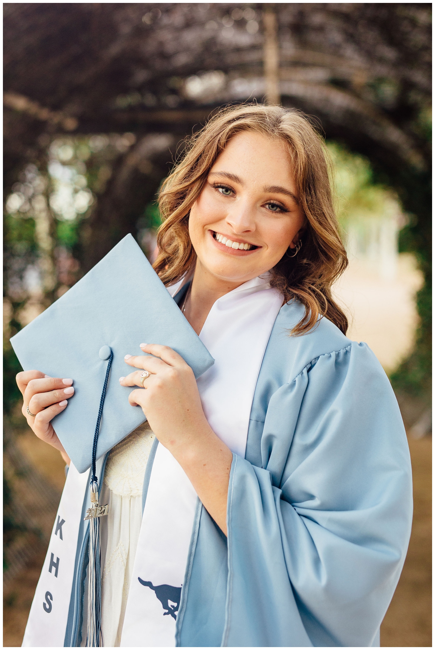 girl holding baby blue grad cap standing in graduation gown senior pictures in Houston