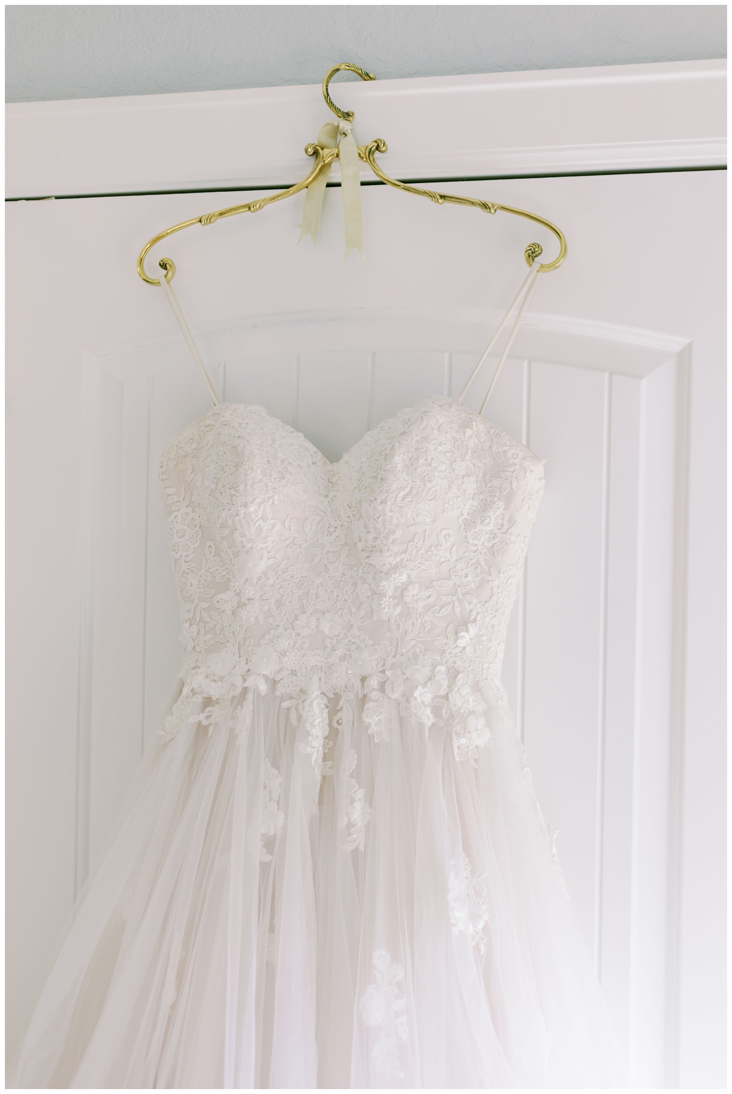 white wedding gown hanging over door with gold hangar