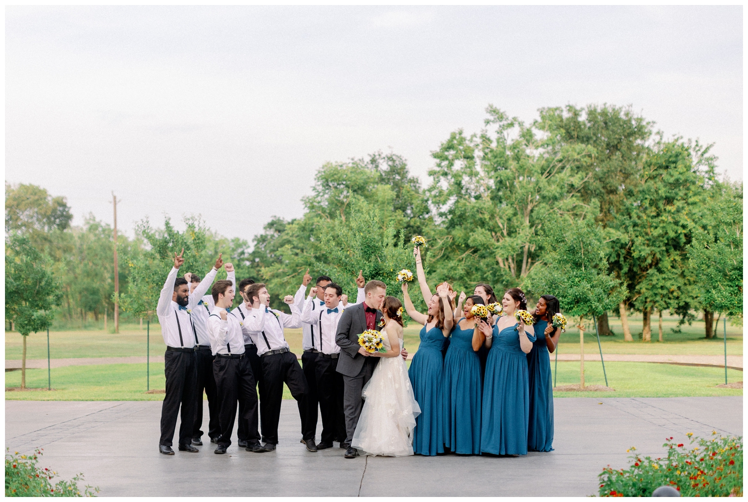 full wedding party portrait with hands in air celebrating bride and groom kissing The Oaks at the Oak Plantation wedding