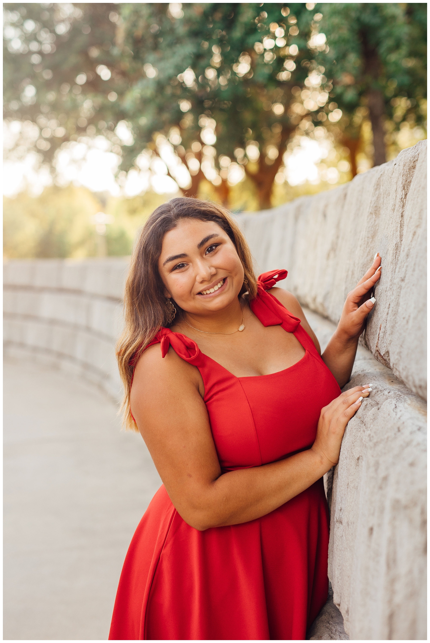 high school senior in red dress leaning on gray wall for best friends senior session in Houston
