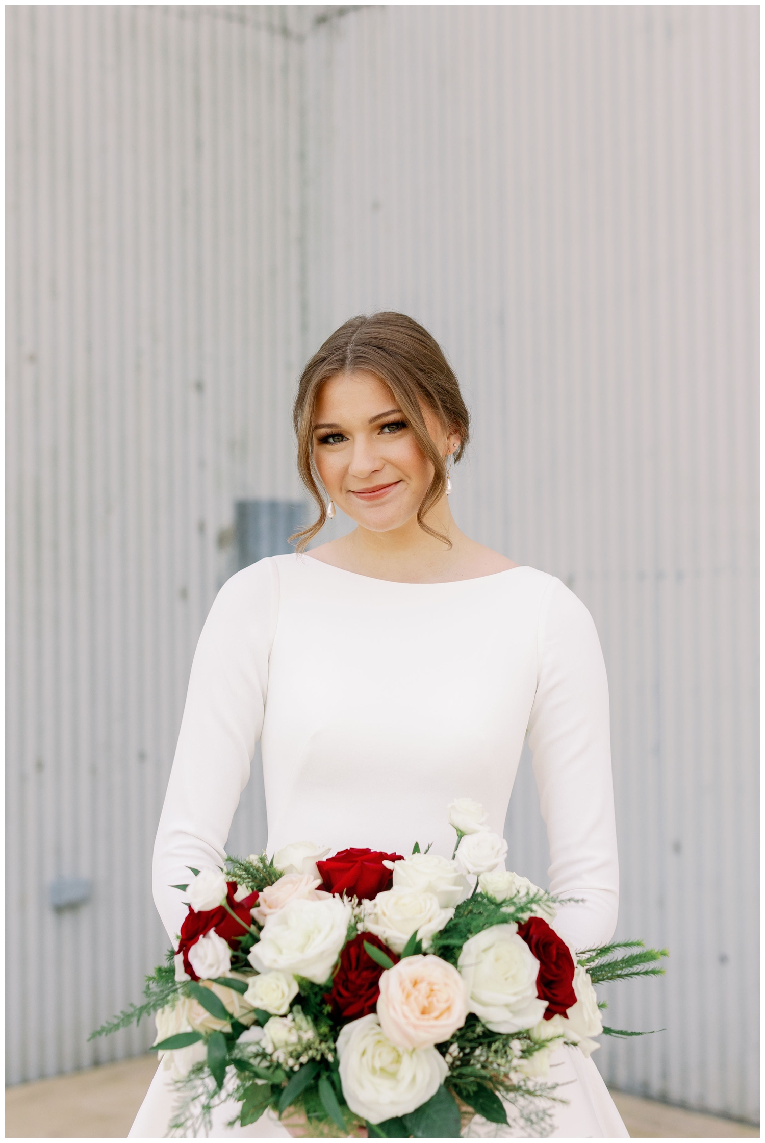 bride in long sleeve wedding gown looking at camera and holding burgundy and white bouquet