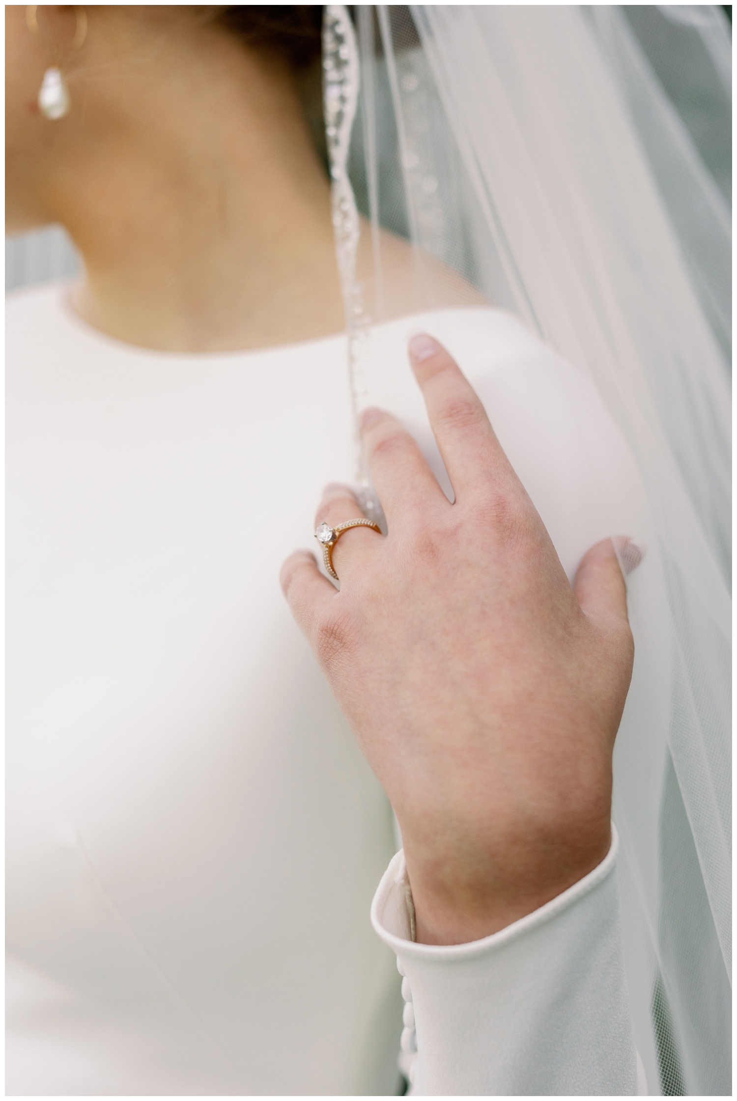 close up image of bride's hand holding her veil with diamond ring