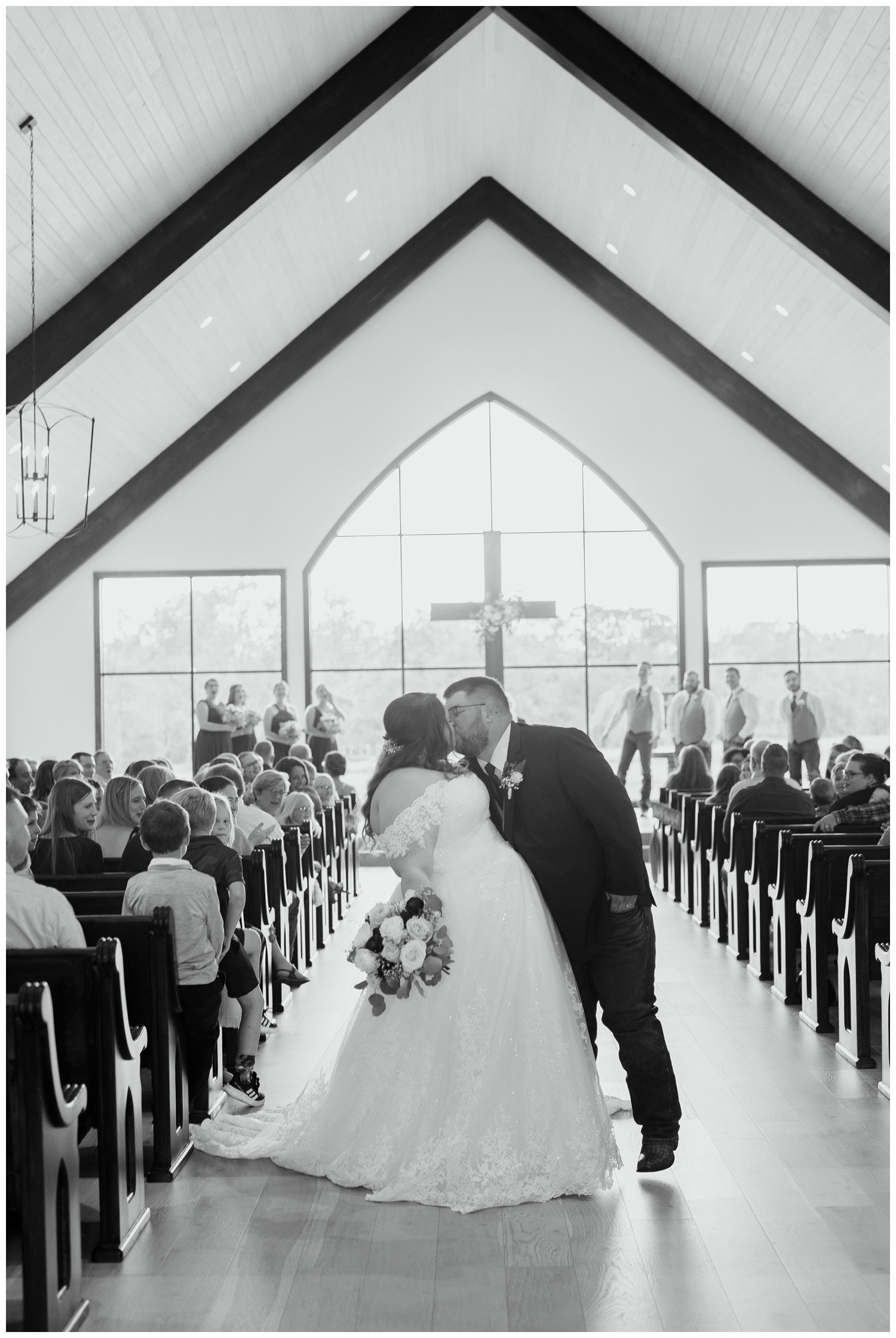 black and white photo of newlyweds kissing during ceremony exit inside chapel at Deep in the Heart Farms wedding venue