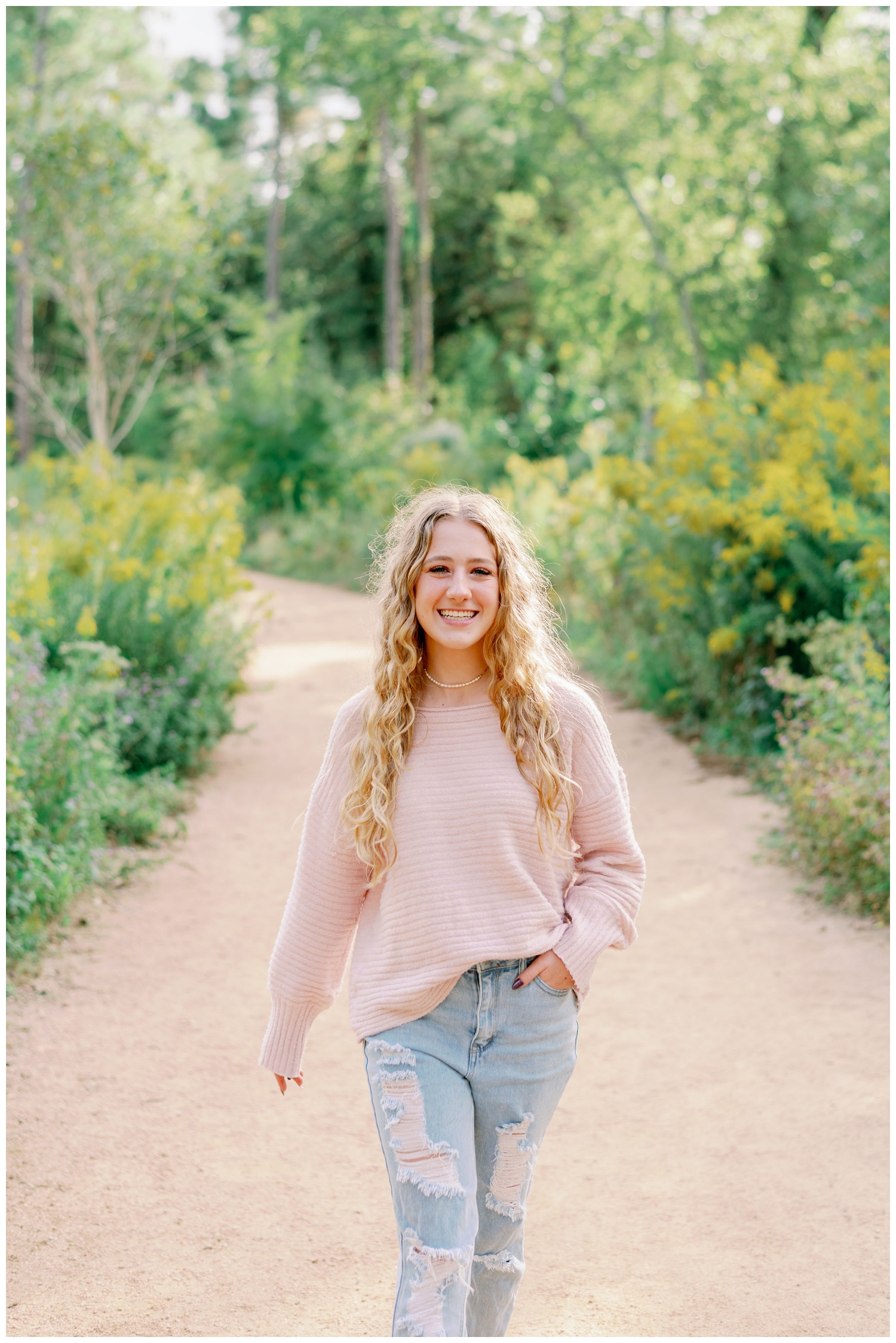 high school senior girl smiling and walking on pathway with flowers