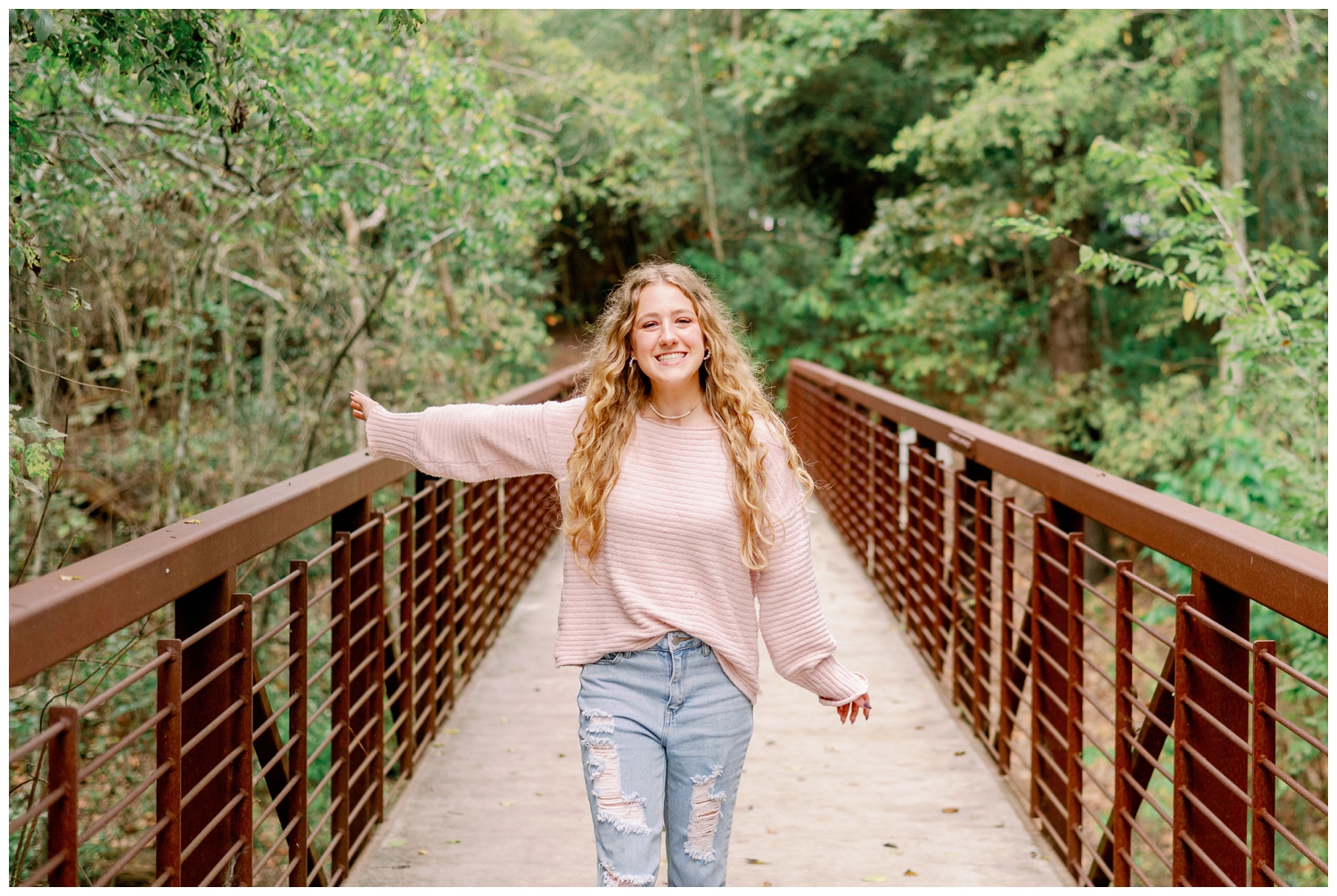 Houston Senior Photography Team girl in pink shirt and denim jeans standing on bridge at Arboretum with hands in air