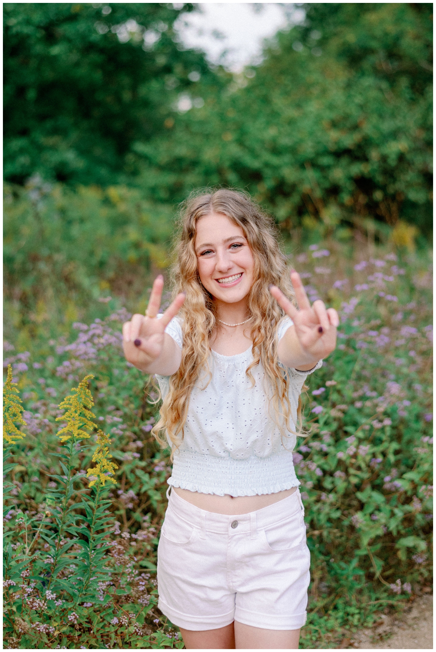 girl in shirt and shirts holding out peace sign with hands in front of flowers at The Houston Arboretum