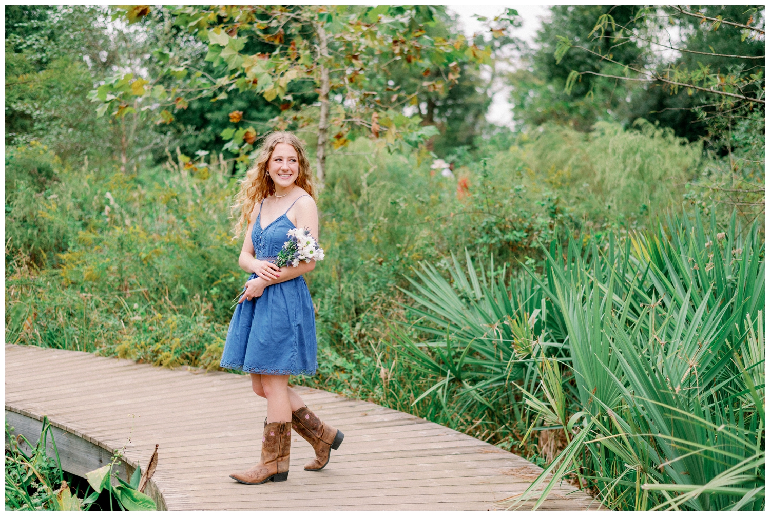 high school senior girl holding flowers and walking on pathway Houston Arboretum