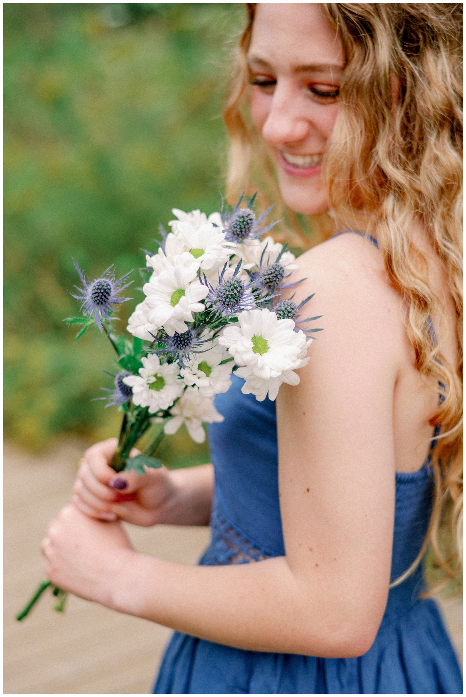 girl in denim dress holding white flowers and looking at them
