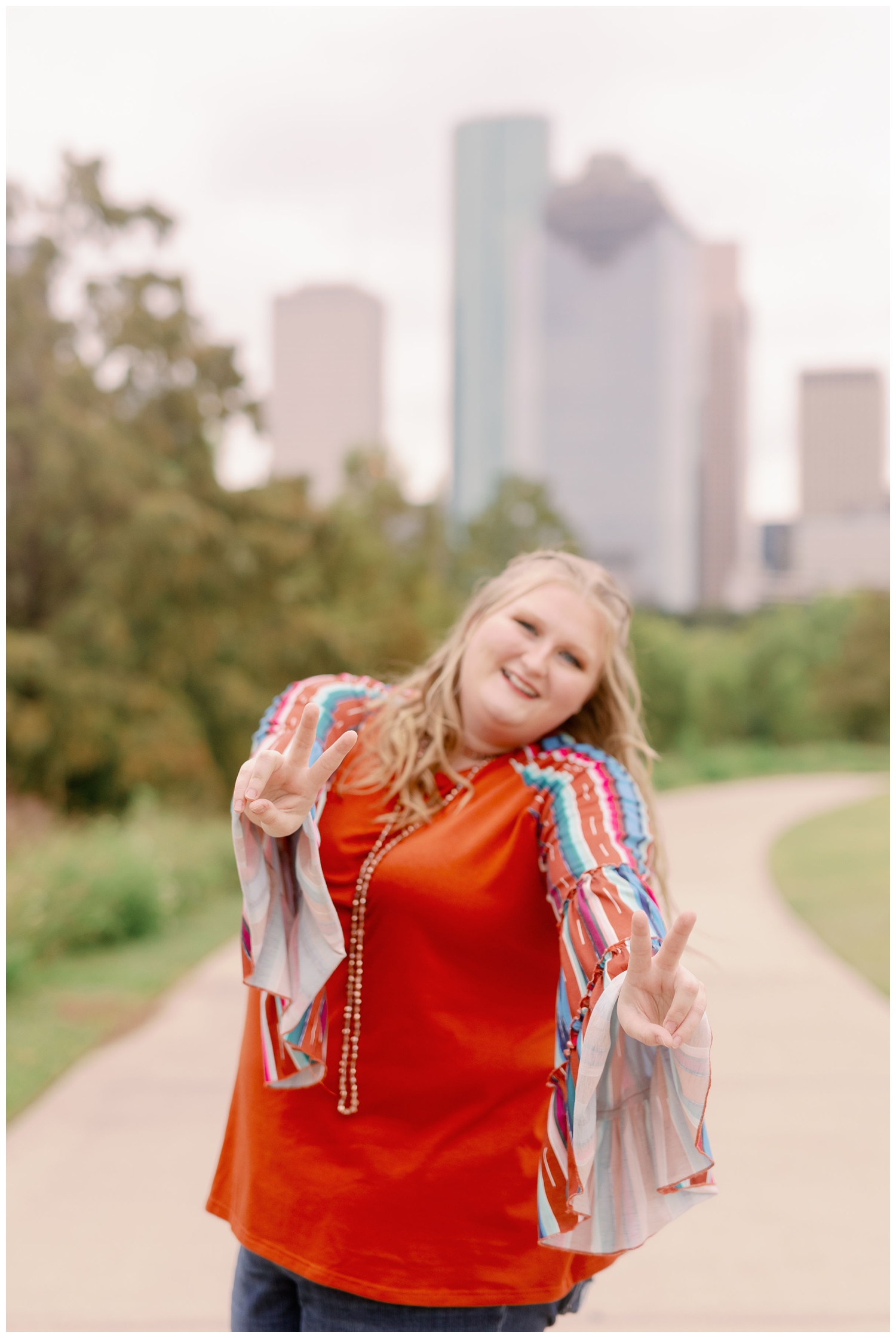 girl in rust striped shirt holding out peace signs senior photos Eleanor Tinsley Park i