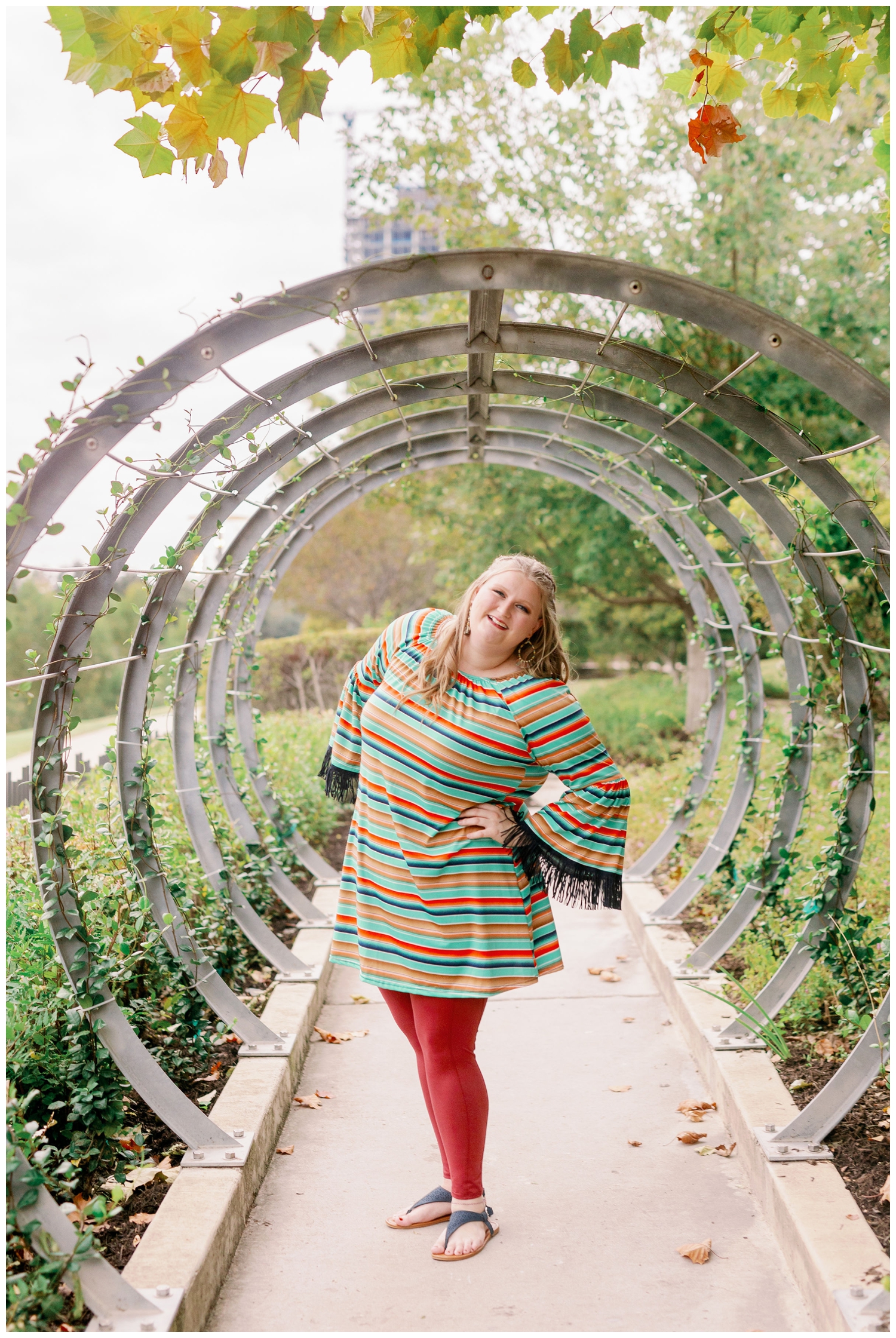 high school senior girl in striped shirt and rust pants standing in between circle arches at Buffalo Bayou