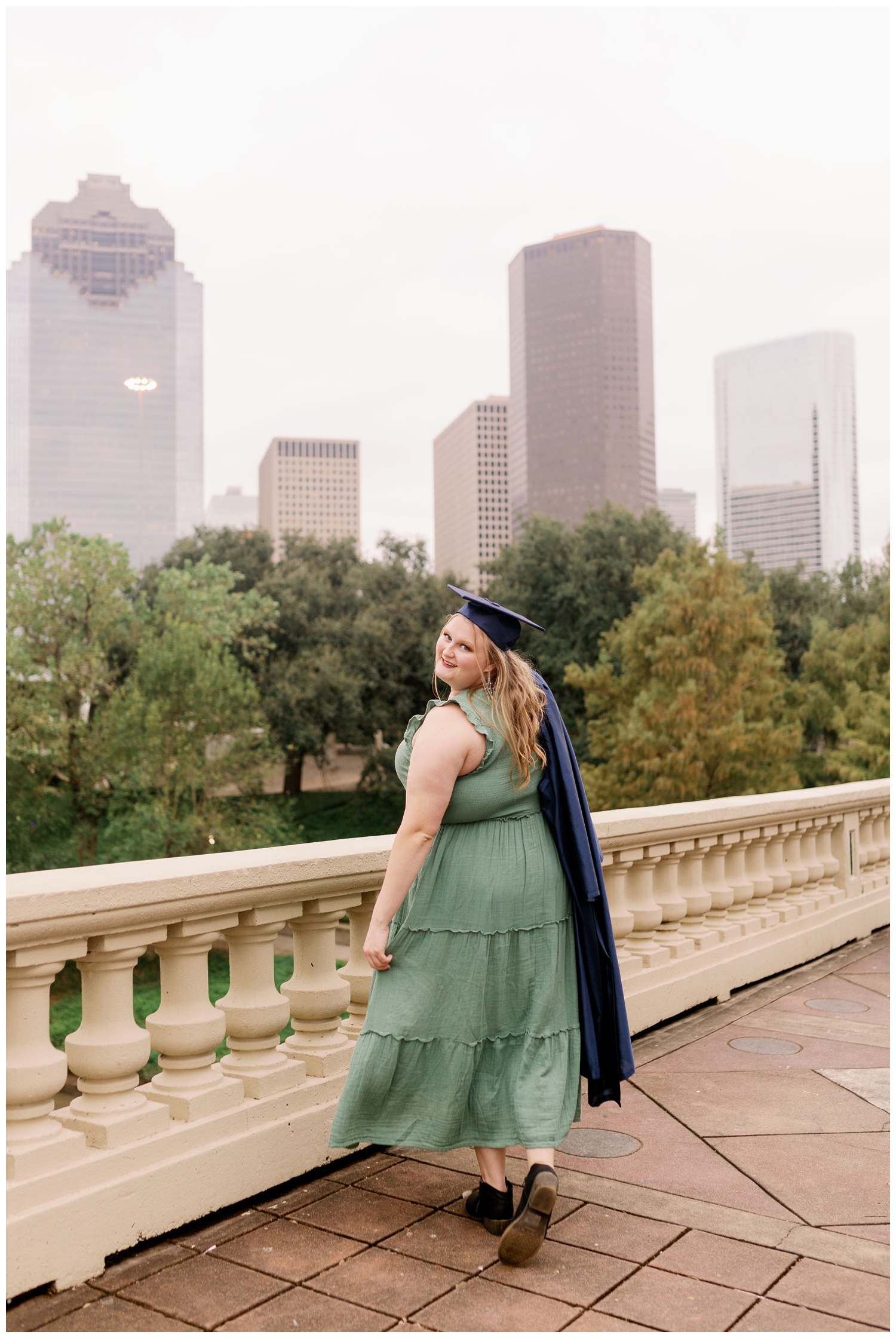 high school senior on Sabine Bridge in front of Houston skyline holding cap and gown