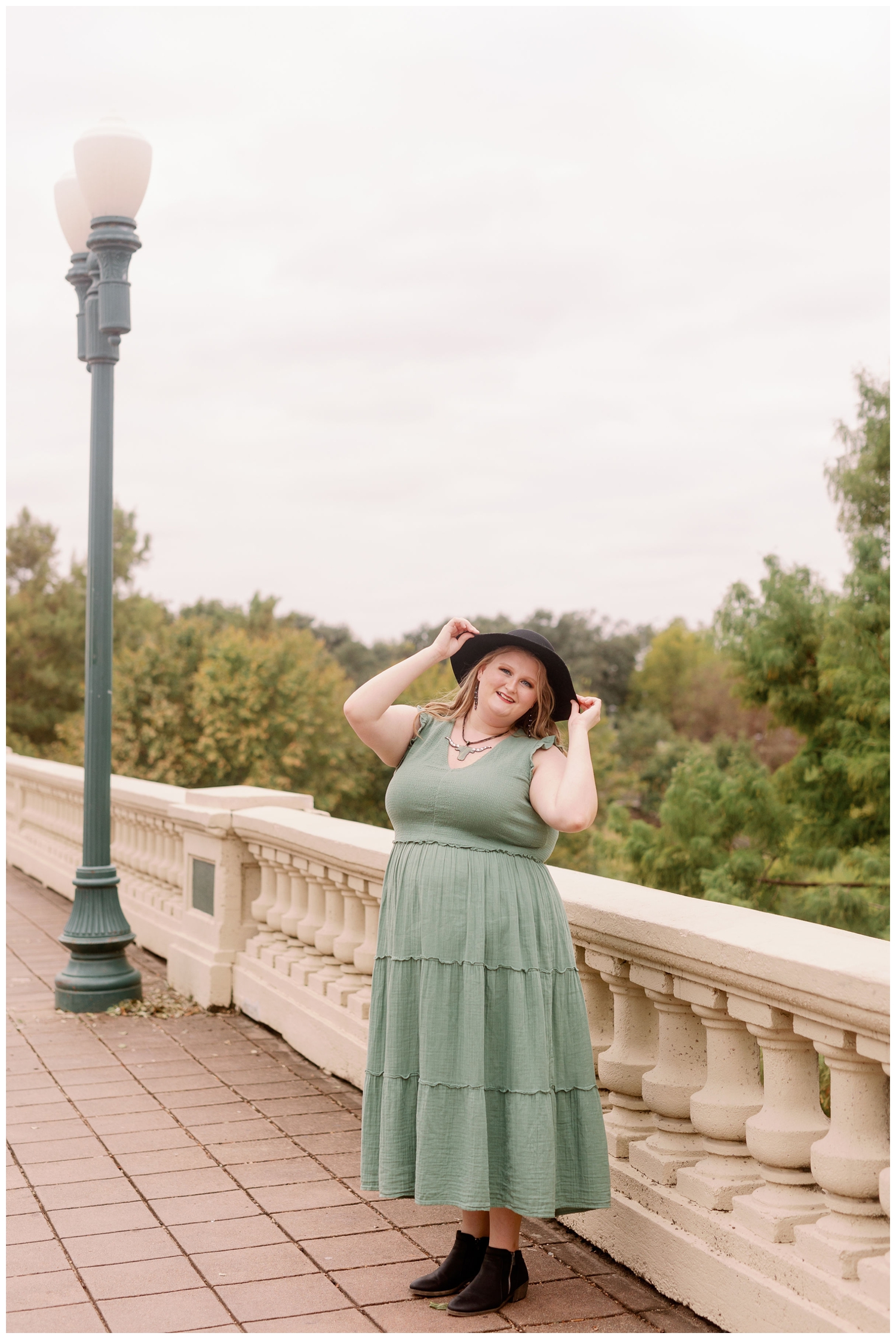 high school senior girl in green sage dress holding a hat on Sabine Street bridge