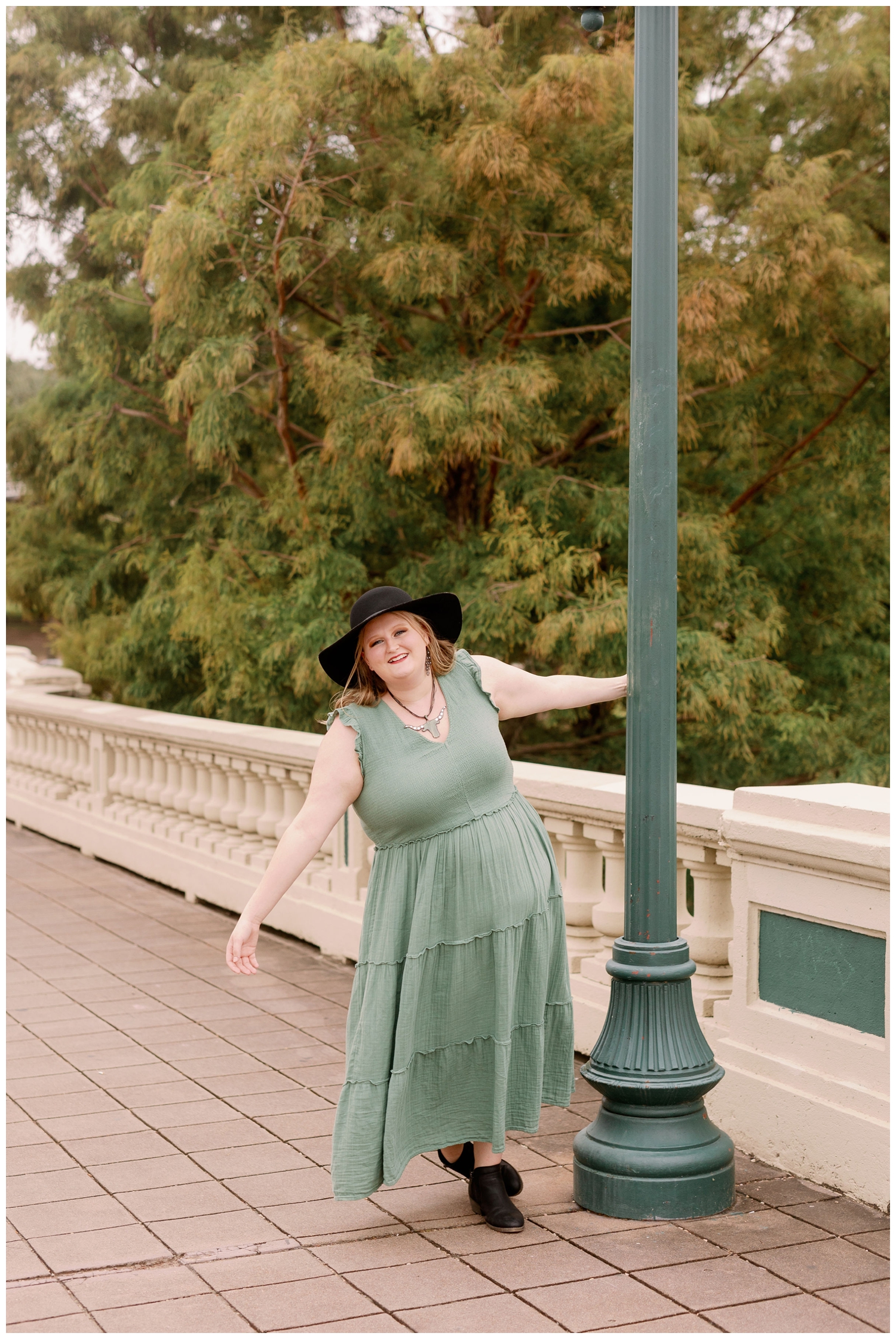 Sabine Street Bridge with high school senior leaning on lamp post in sage green sundress and black hat
