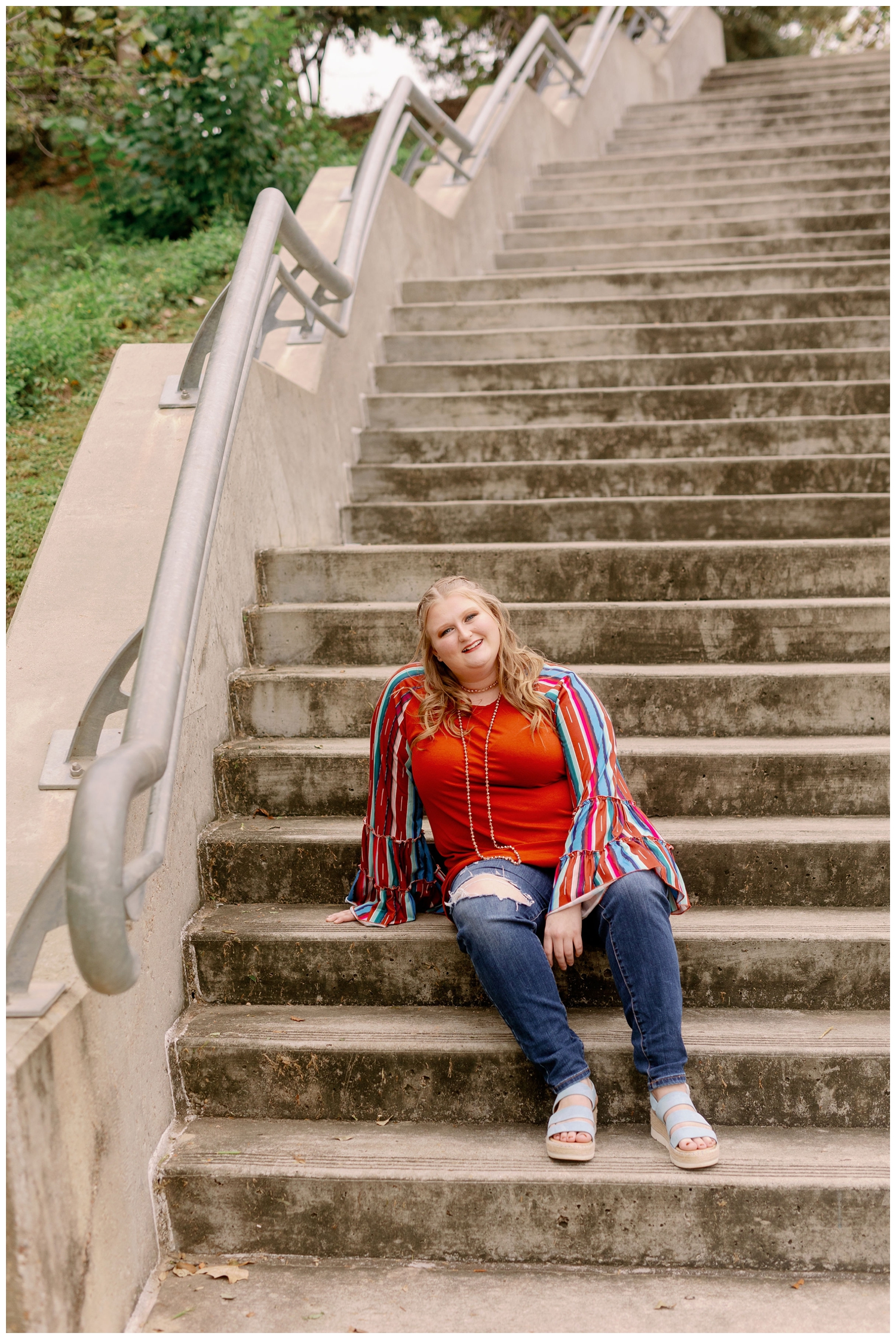 girl in jeans and colorful shirt sitting on staircase at senior photos Eleanor Tinsley Park in Houston