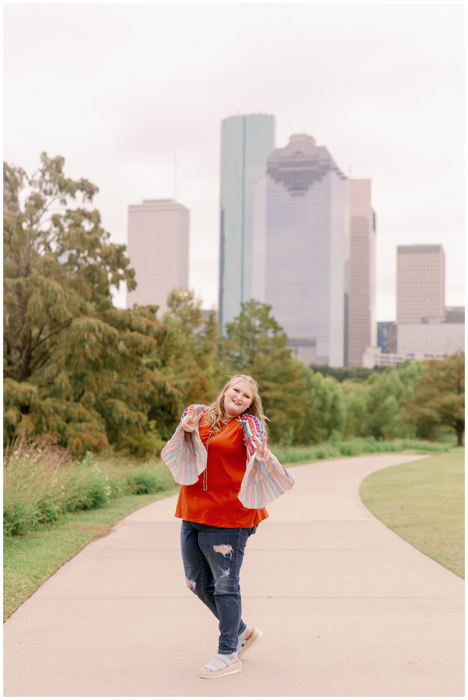 senior girl holding out peace signs with hand in front of Houston skyline