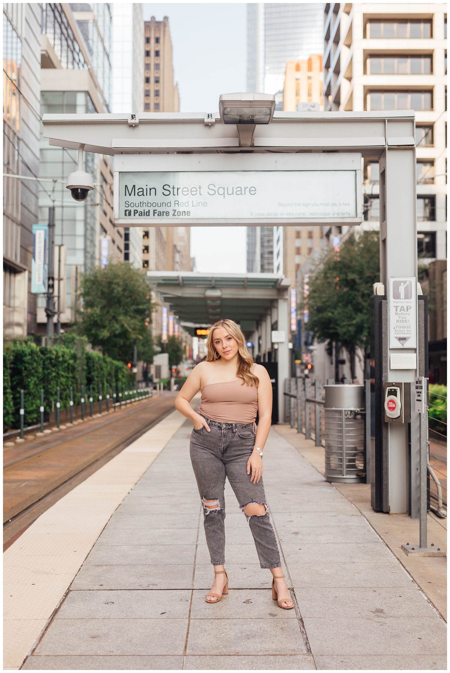 high school girl in black jeans and tan tank shirt standing in front of Main Street Metro Rail station downtown Houston