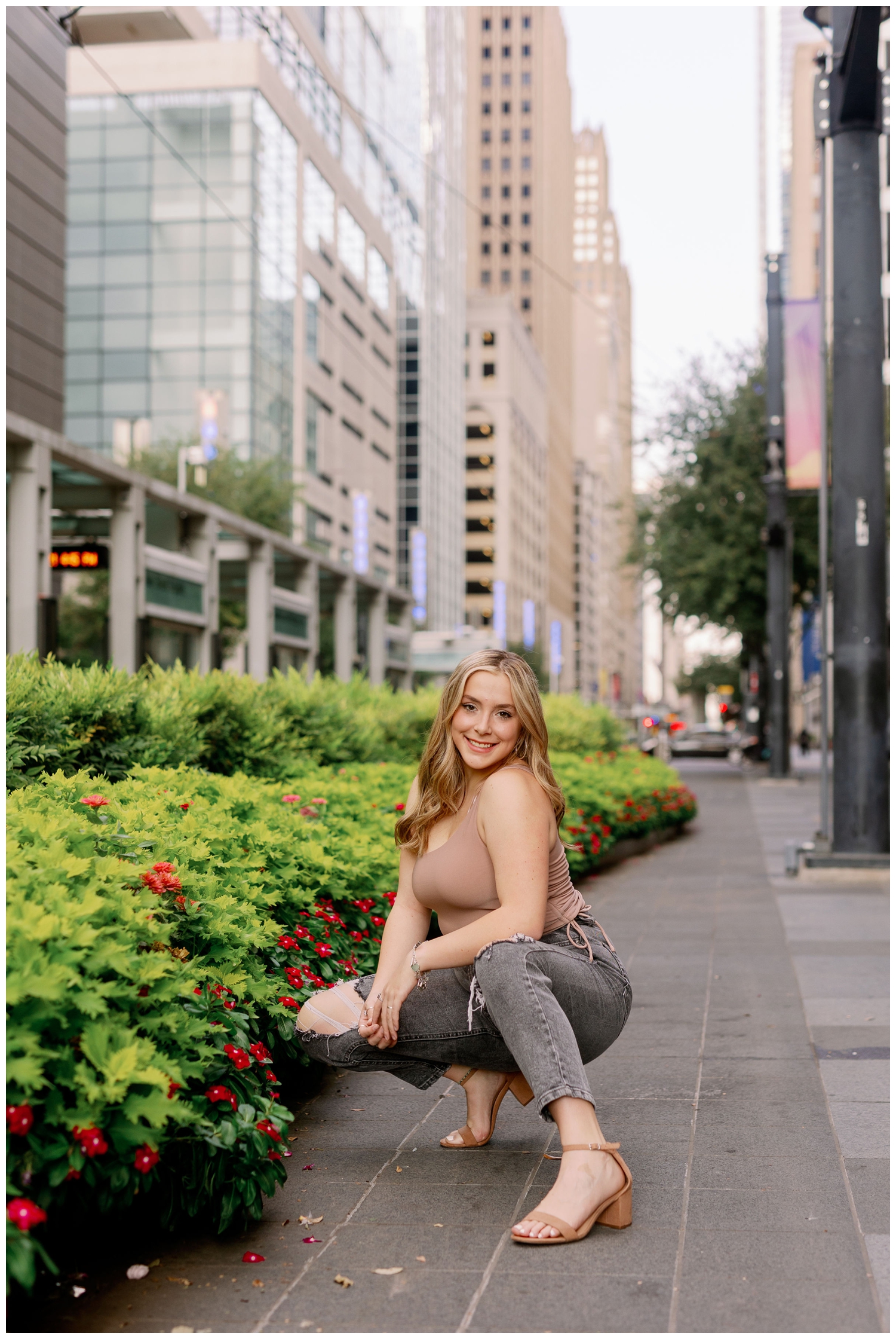 high school senior girl in black jeans and tan tank shit squatting by green plants in downtown Houston