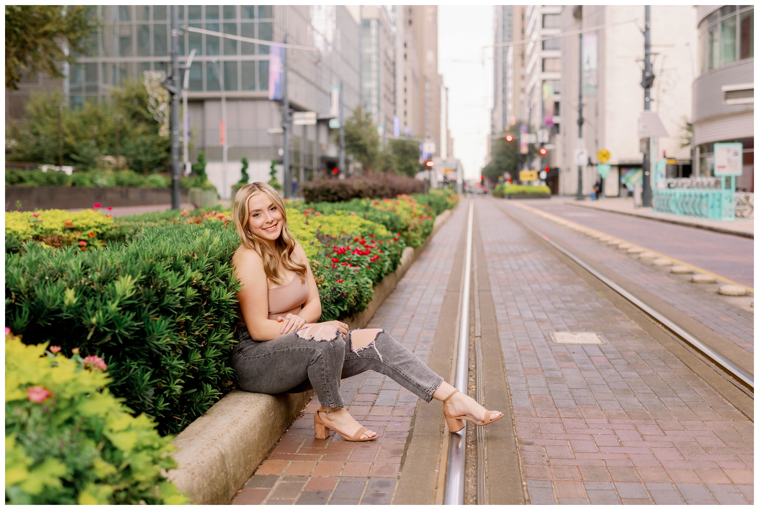 girl sitting on curb downtown in front of buildings senior photos Main Street Houston