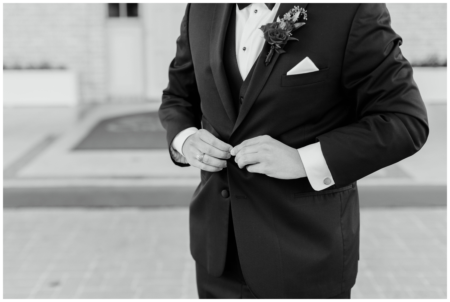 black and white detailed shot of groom fastening tux jacket outside Sugar Creek Country Club