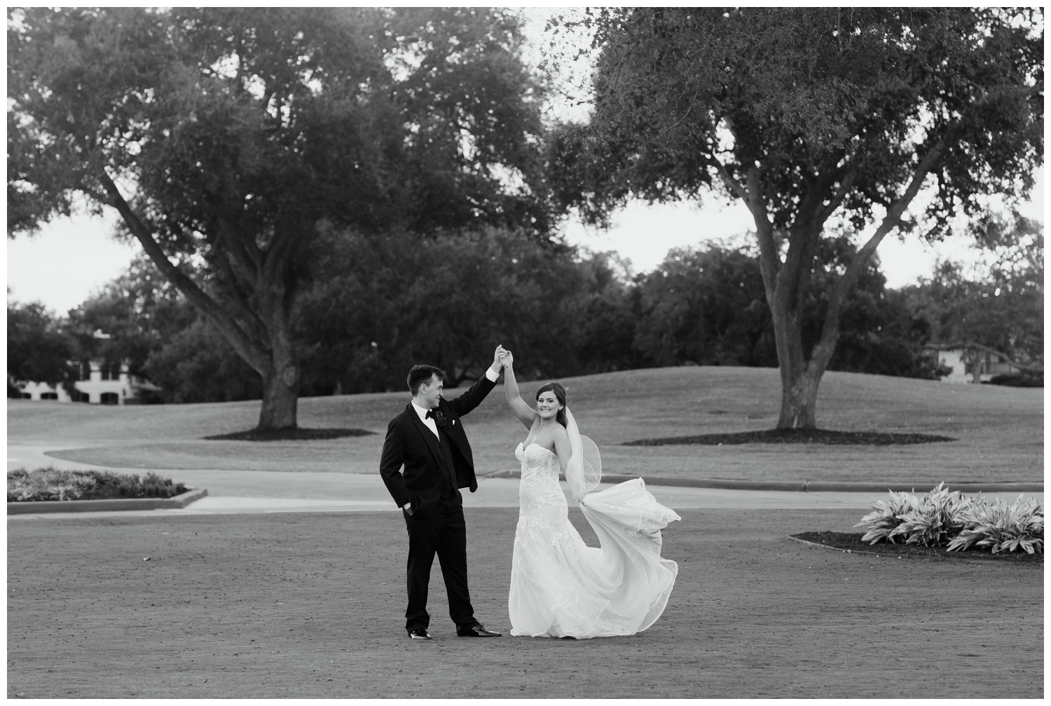 black and white photo of groom twirling bride with dress flowing outdoors at Sugar Creek Country Club wedding