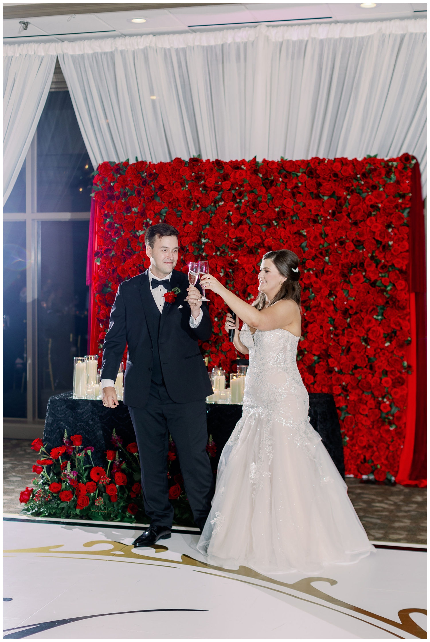 bride and groom toasting standing in front of sweetheart table and rose wall
