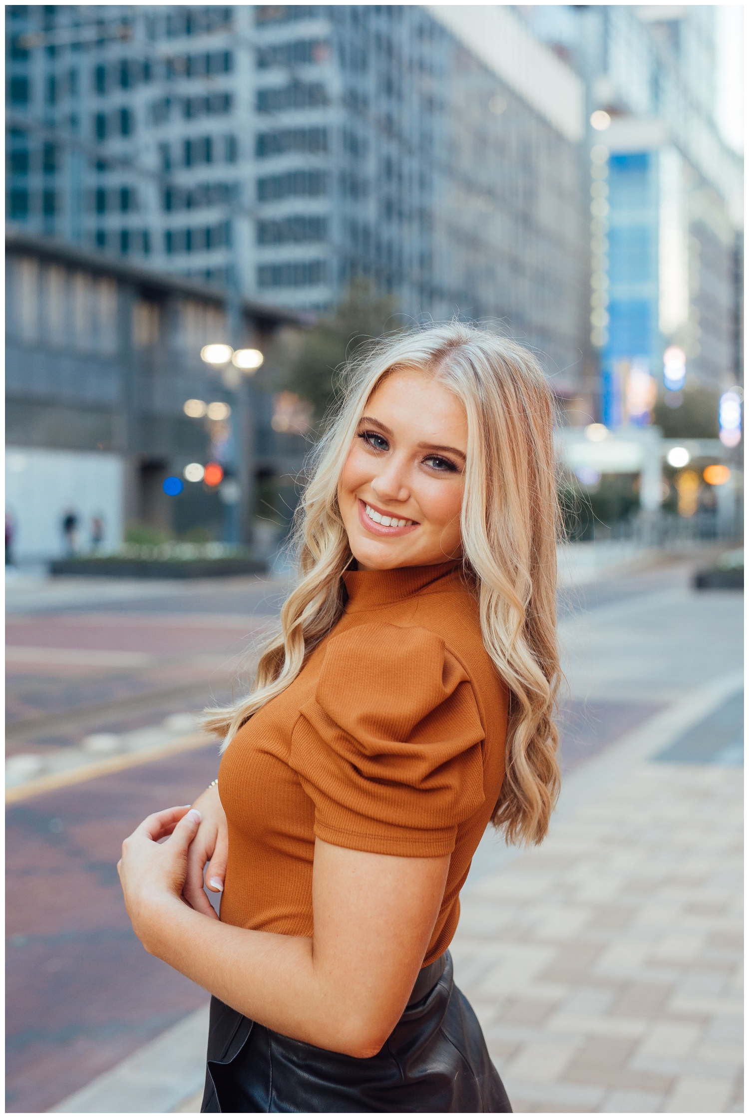 senior pictures Main Street with blonde high school senior smiling at camera with hands clasped by waist