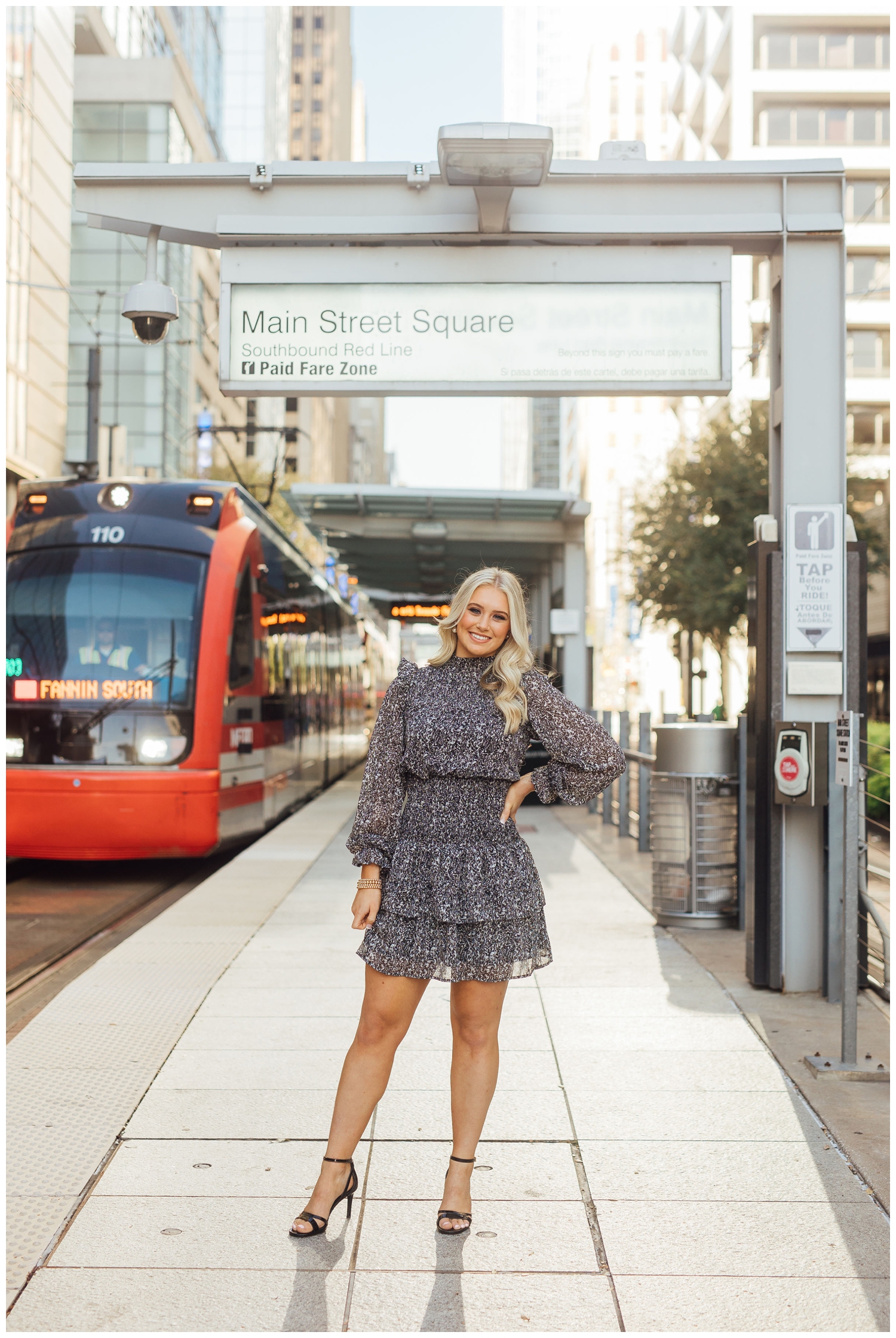 high school senior standing in front of Main Street METRORail station in downtown Houston with hand on hip in black dress