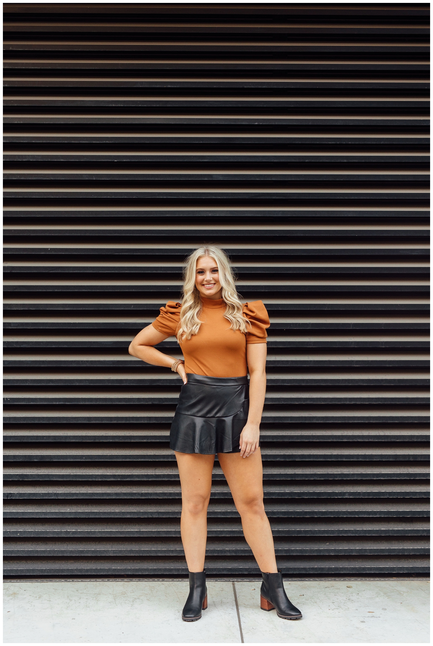 high school senior girl in black skirt and rust shirt standing in front of black wall