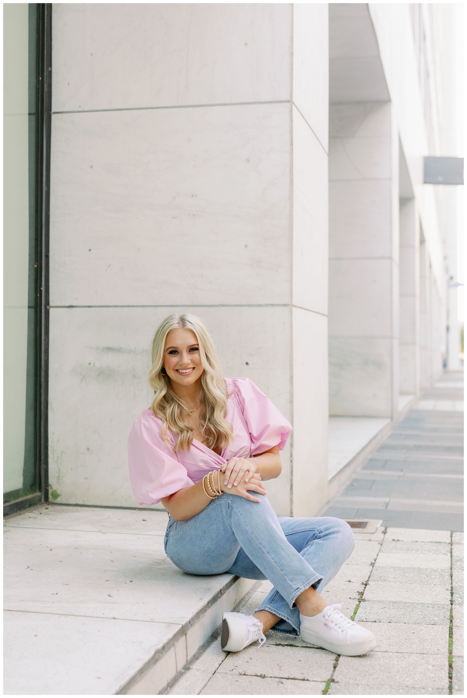 high school senior sitting on ground in jeans and pink shirt for senior pictures Main Street Houston