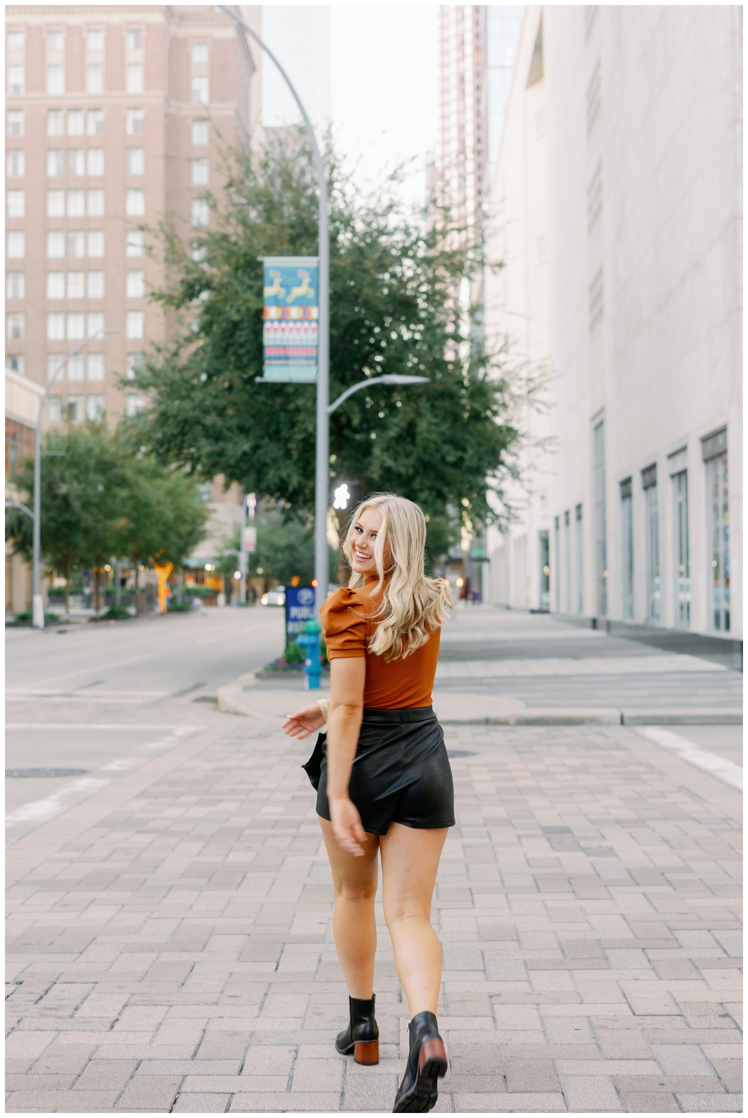 high school senior girl in black shorts and rust shirt smiling and walking across Main Street downtown Houston