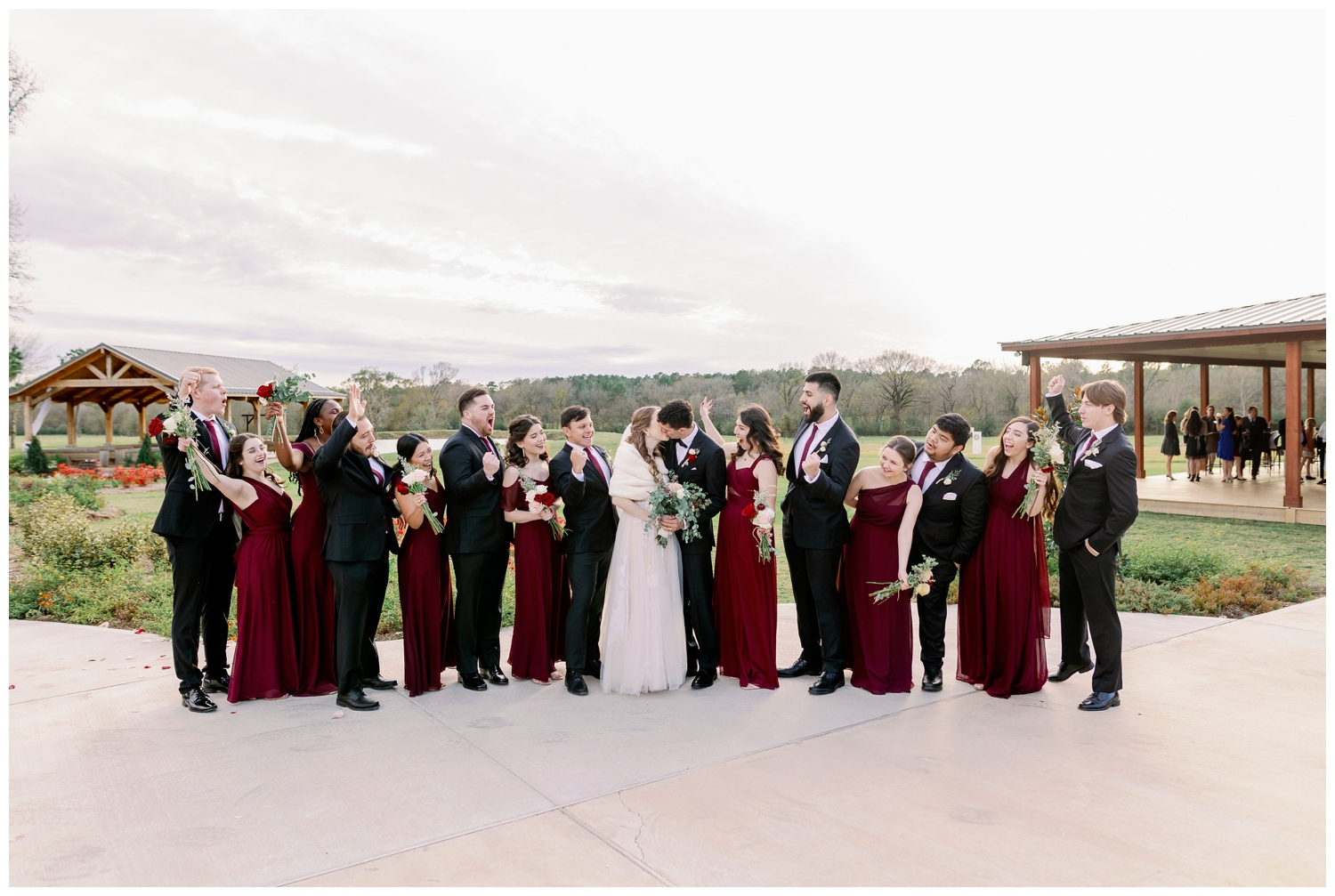bride and groom kissing surrounded by full bridal party in burgundy and black at winter Union Ranch Wedding