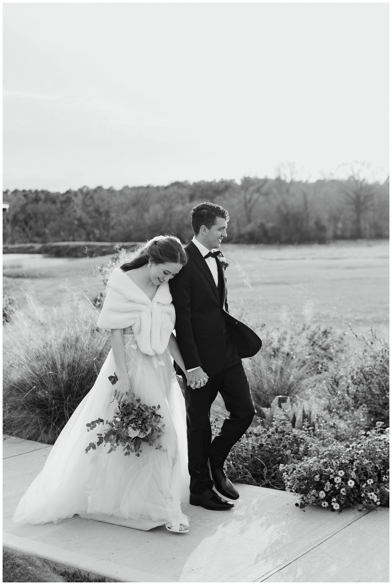 black and white image of bride and groom holding hands walking