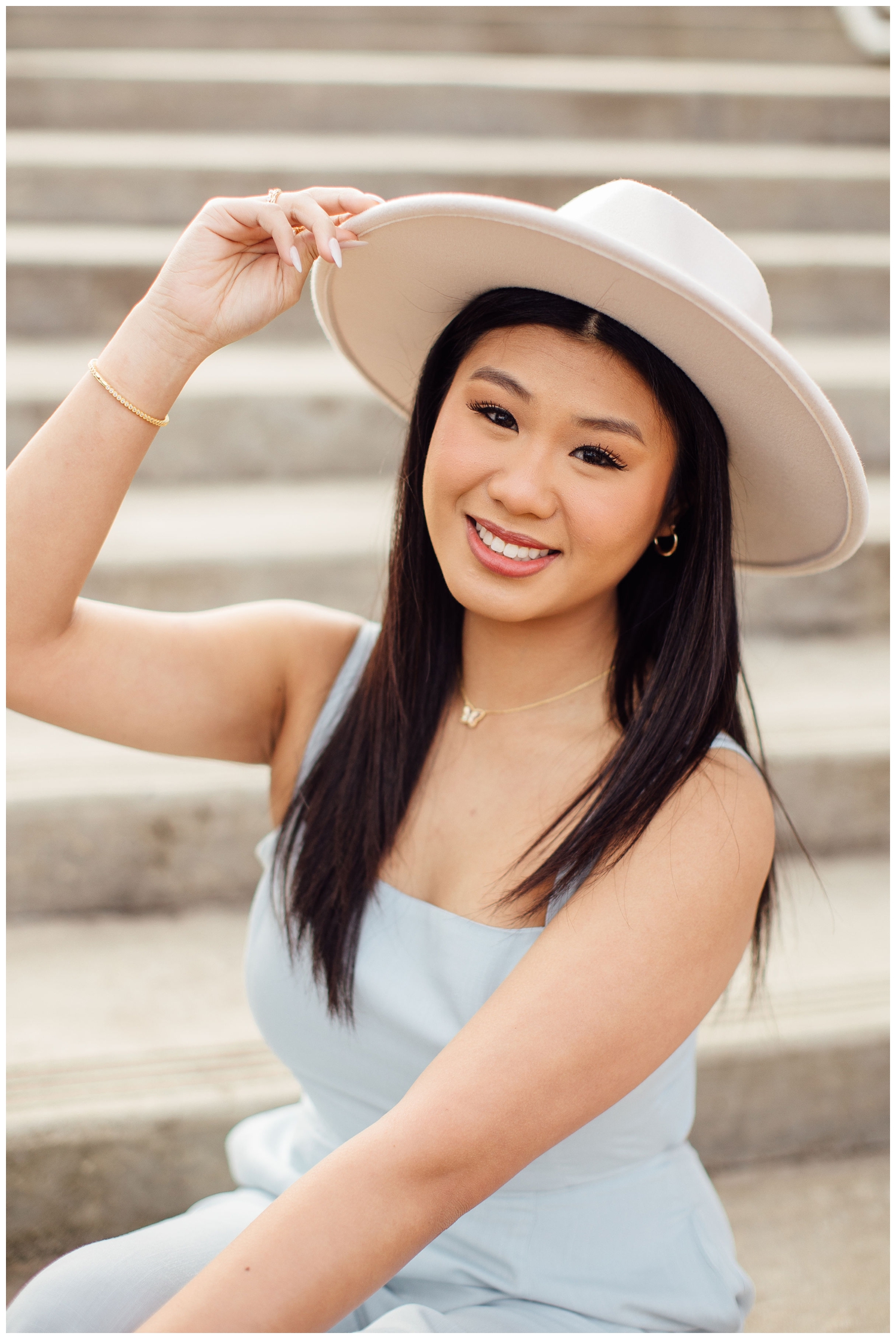 high school senior girl sitting on stairs with hand on white hat