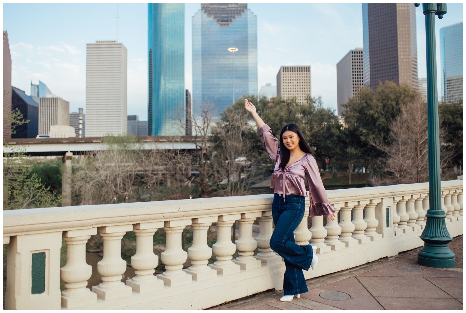 girl in jeans and plumb shirt holding hands in air for Houston senior photos downtown