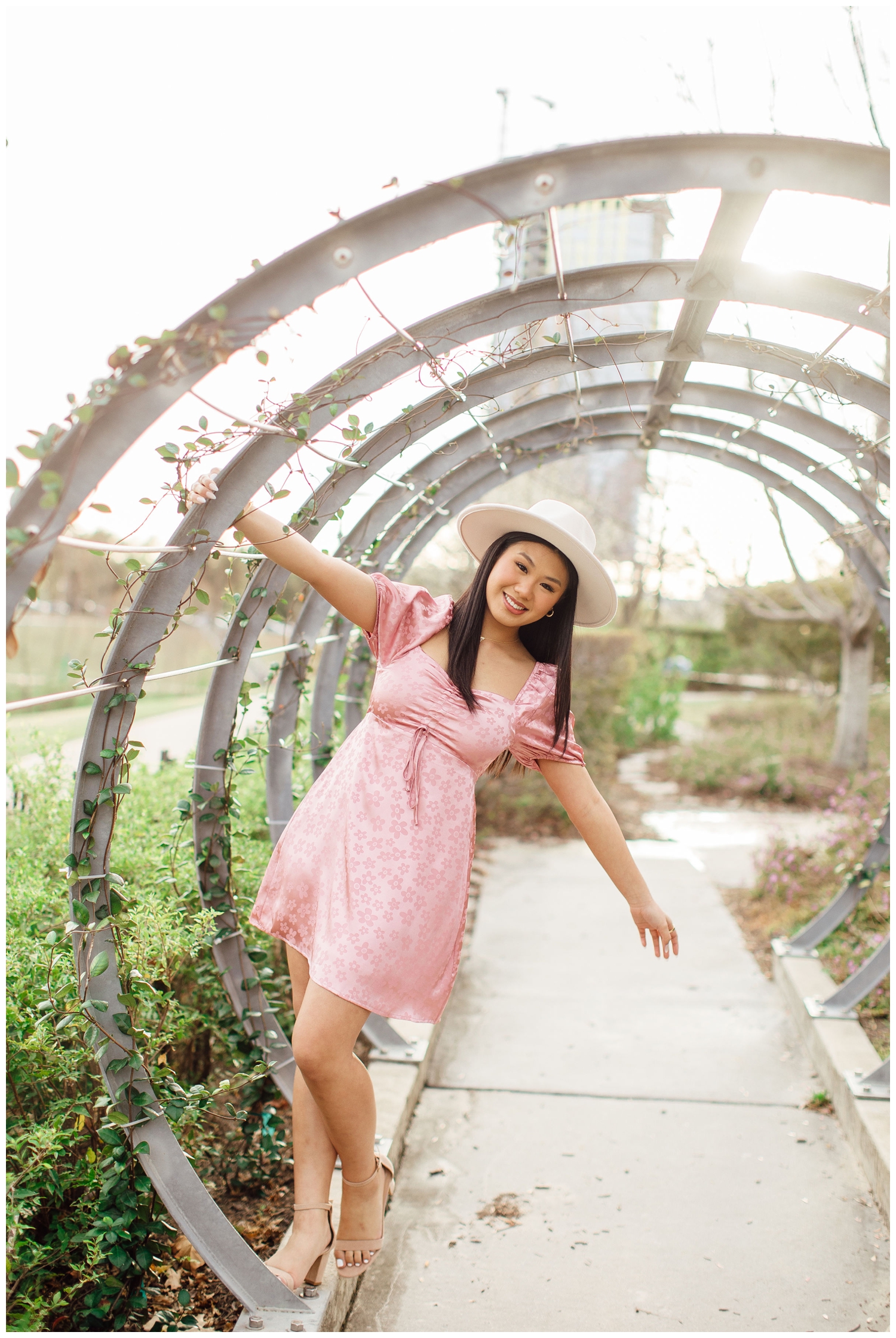 senior girl in pink dress hanging on garden rings