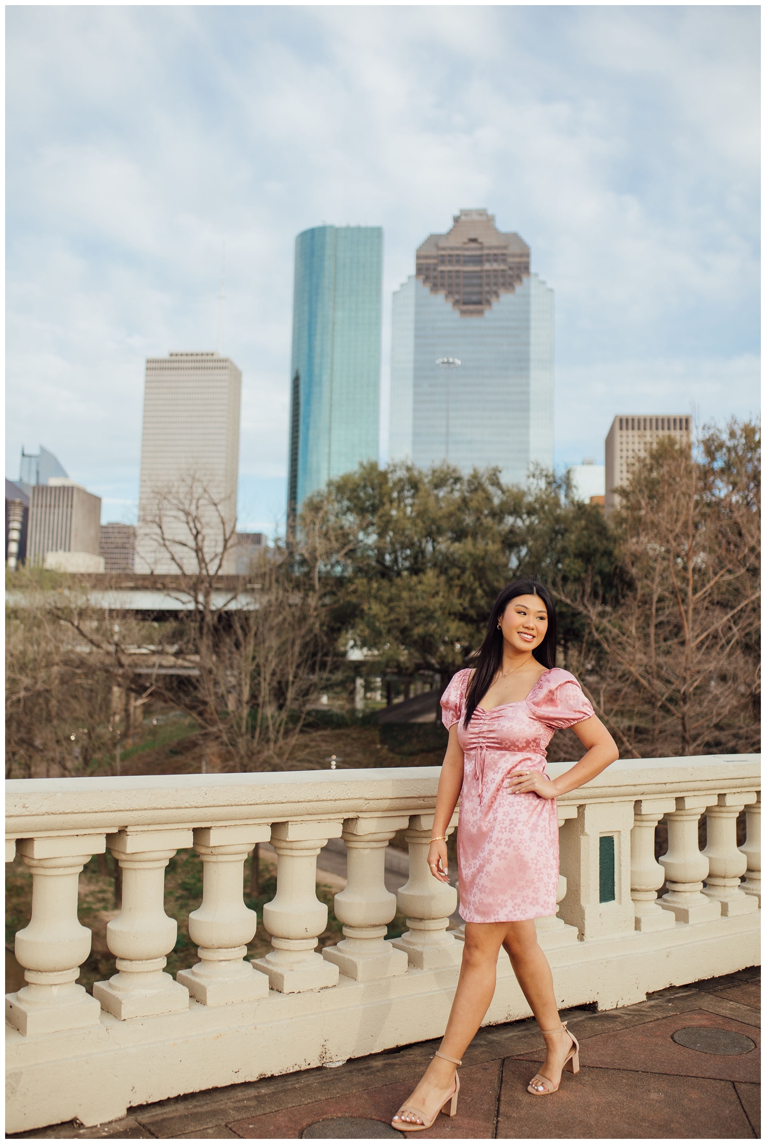 chic Houston senior photos with girl in pink dress standing in front of Houston skyline