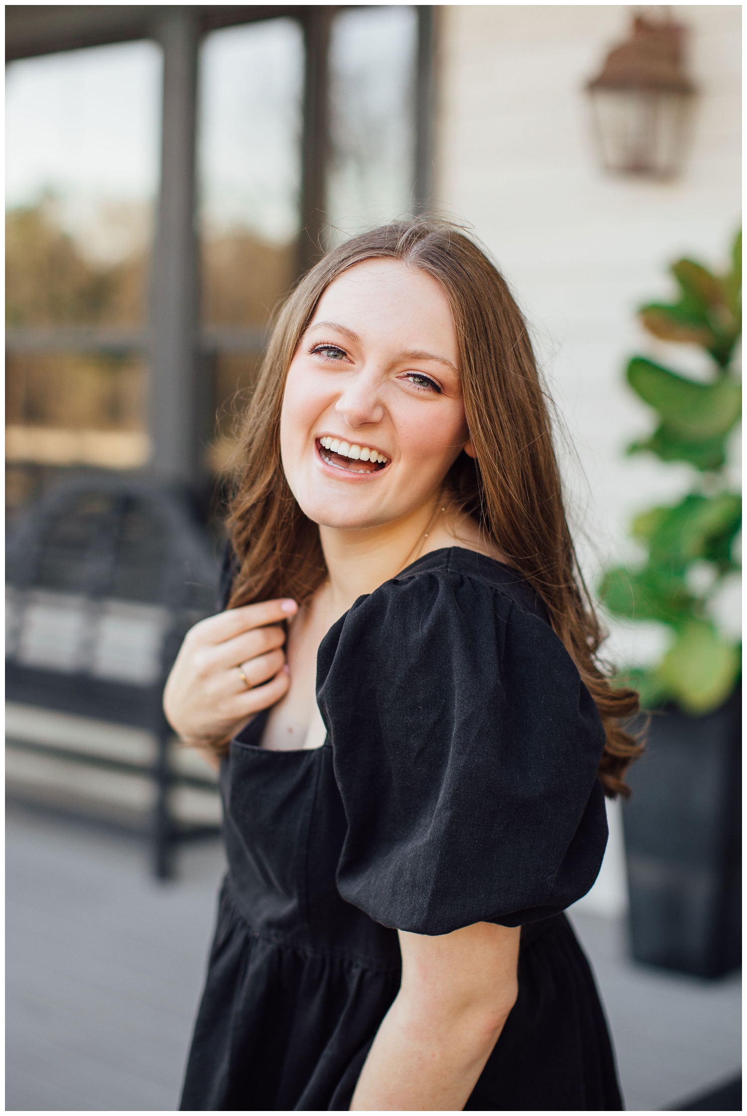 high school senior with hand in hair laughing in black dress